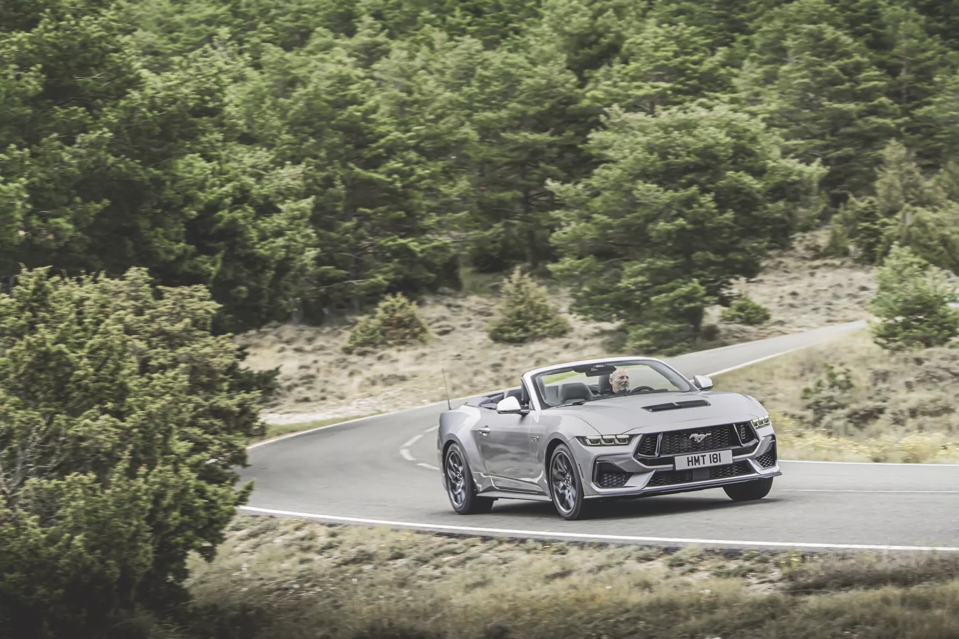 Ford Mustang cabriolet 2024 en mouvement sur route sinueuse, présentant la façade avant, le capot et le profil latéral avec un design aérodynamique, phares LED et grandes roues en alliage