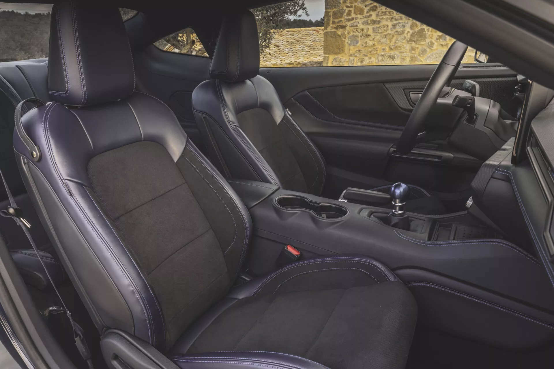Vue détaillée de l'intérieur de la Ford Mustang 2024 mettant en avant des sièges sport en cuir de haute qualité, un levier de vitesse manuel et la console centrale depuis la perspective de la porte du conducteur