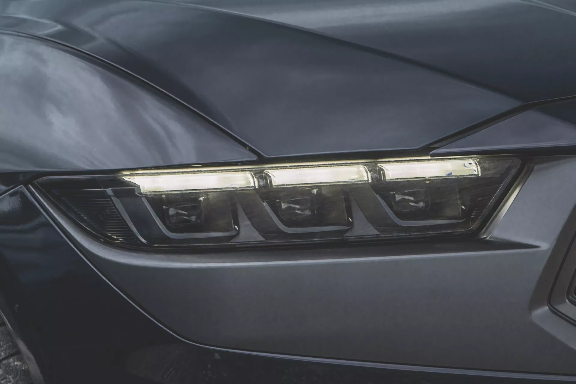 Gros plan sur le phare côté conducteur de la Ford Mustang 2024, illustrant la technologie moderne LED ou HID et un design aérodynamique dans une finition de couleur foncée.