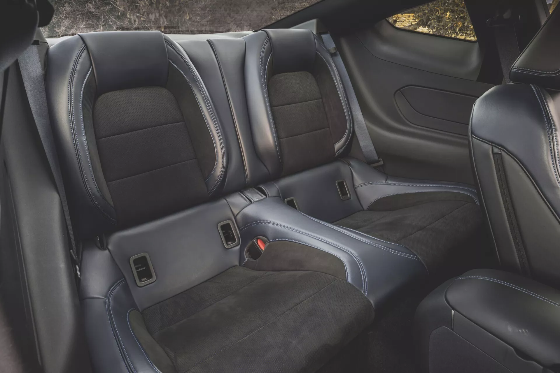Zone de sièges arrière intérieurs Ford Mustang 2024 (2ème Génération) avec sellerie en cuir noir, coutures détaillées, sièges baquets profilés, accoudoir repliable avec porte-gobelet - Vue de dessus