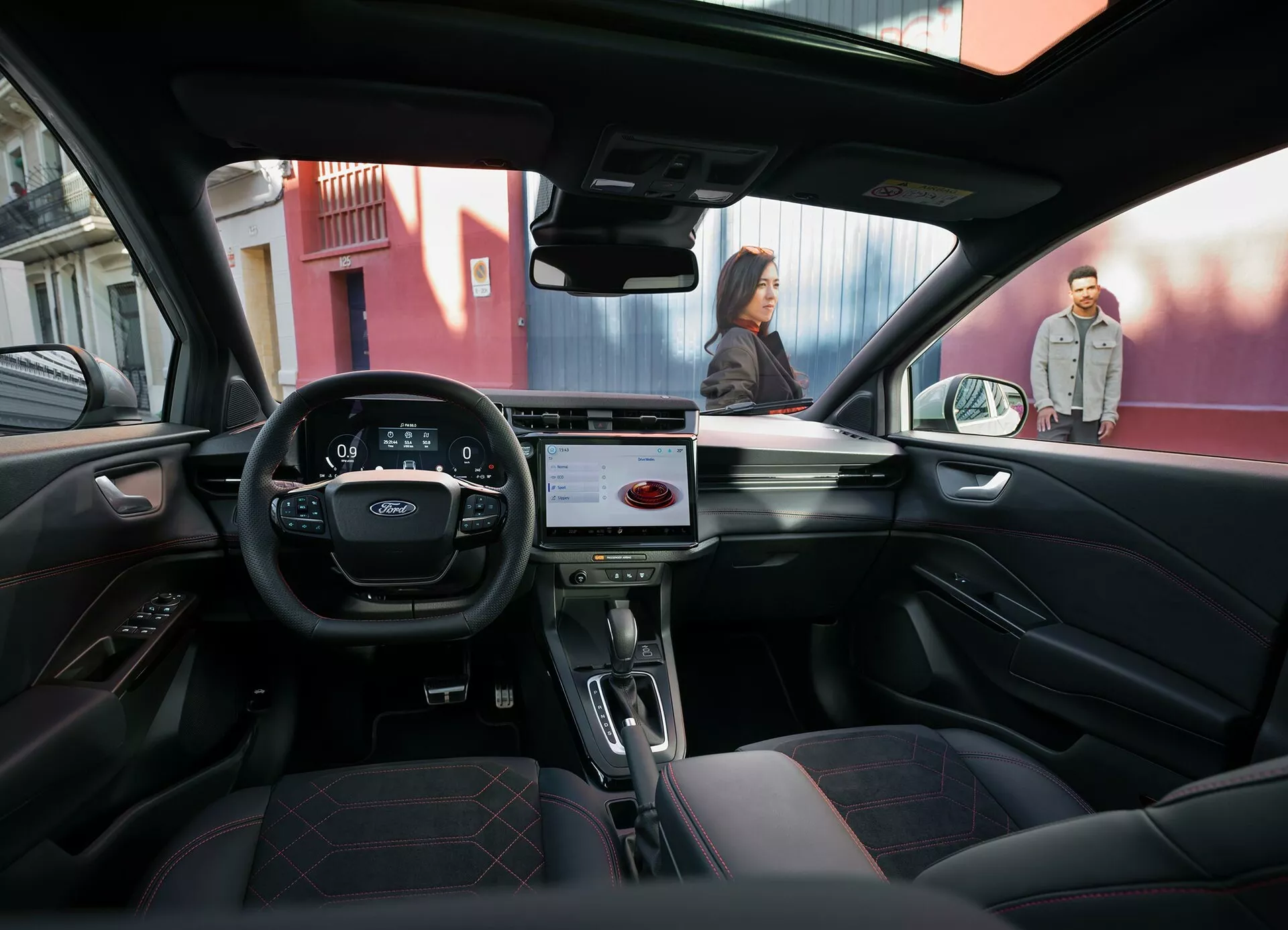 Vue intérieure depuis le siège arrière d'une Ford Puma 2024 montrant le tableau de bord avec système d'infodivertissement tactile, sièges avant en cuir, volant avec commandes et vue extérieure urbaine à travers le pare-brise