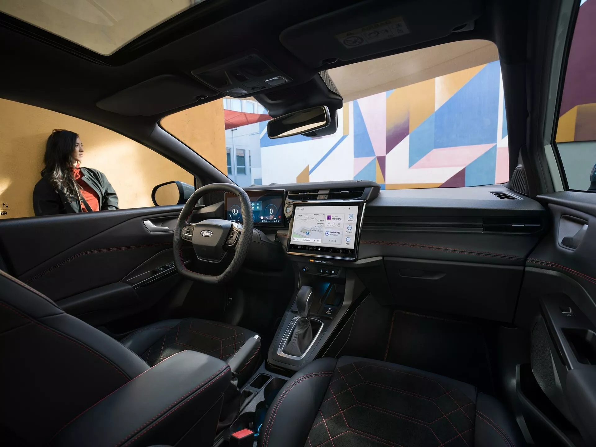 Vue intérieure du Ford Puma 2024 facelift depuis la perspective d'un passager arrière montrant volant multifonctions en cuir, tableau de bord numérique, grand système d'infodivertissement tactile, levier de vitesse automatique sur la console centrale, sièges en cuir matelassé, et toit ouvrant