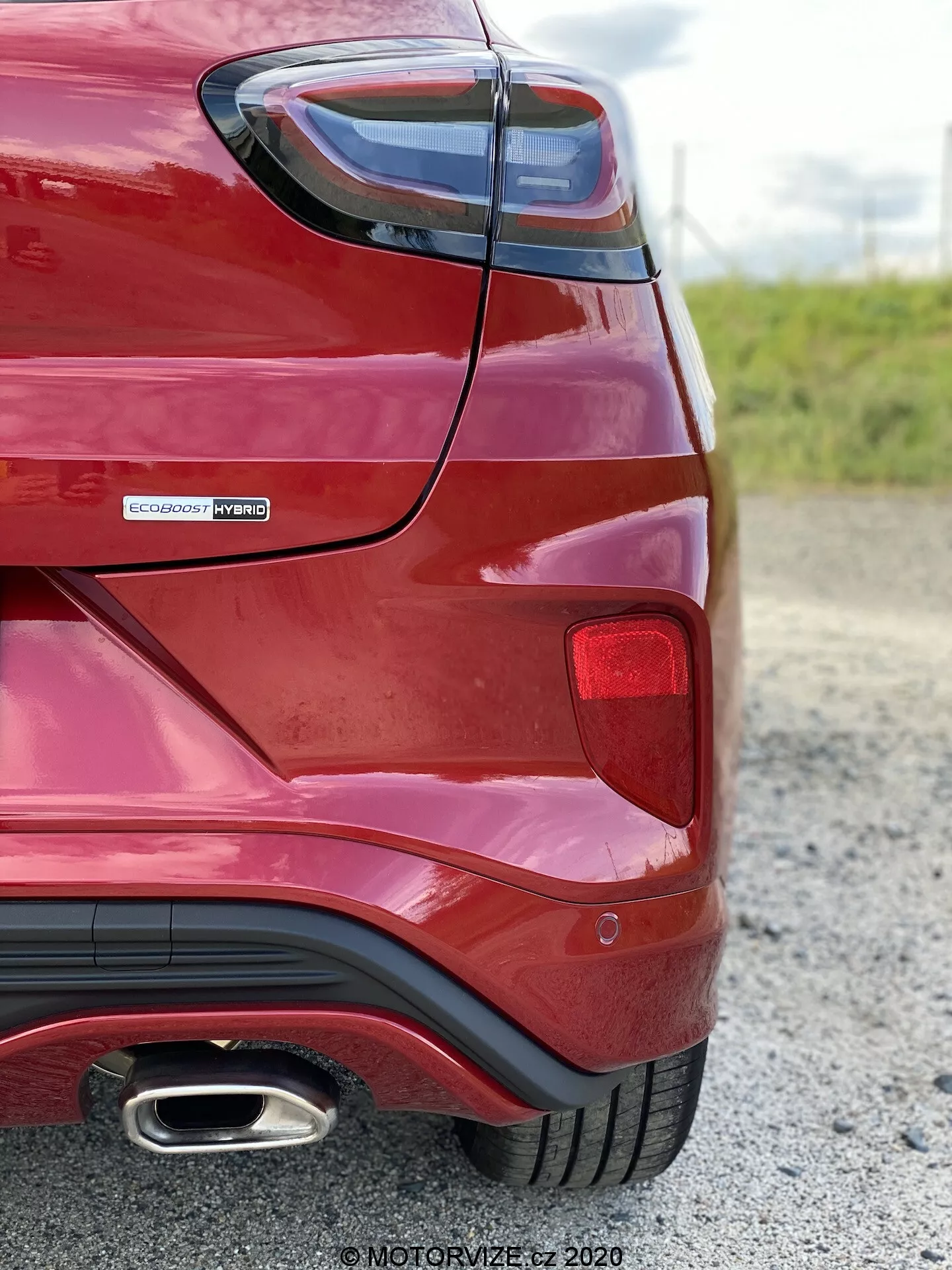 Vue d'angle arrière d'une Ford Puma 2020 rouge prise de près et sous un angle bas, mettant en valeur la courbure de l'aile arrière, l'assemblage des feux arrière, le badge EcoBoost Hybrid indiquant un groupe motopropulseur hybride et l'embout d'échappement chromé unique. Soulignant des éléments de design modernes tels que les feux arrière angulaires et le pare-chocs arrière aérodynamique avec un style diffuseur.