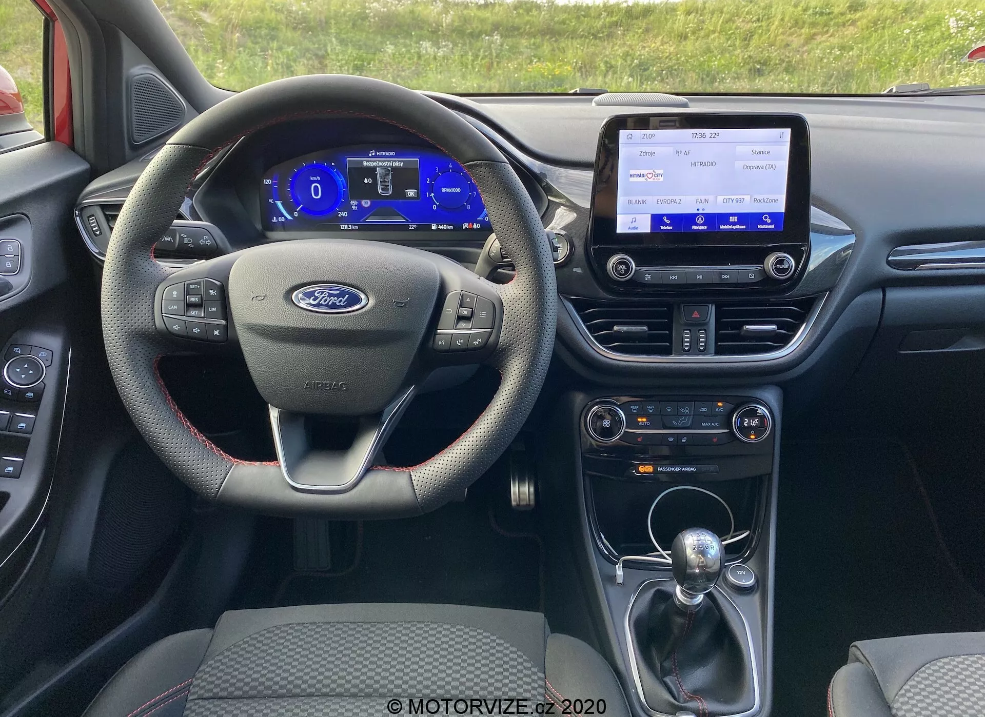 Vue intérieure de la Ford Puma 2020 depuis la perspective du conducteur, montrant le volant multifonctions à trois branches, le tableau de bord numérique, la console centrale infotainment avec fonctions de connectivité, le levier de changement de vitesse automatique et divers systèmes de contrôle