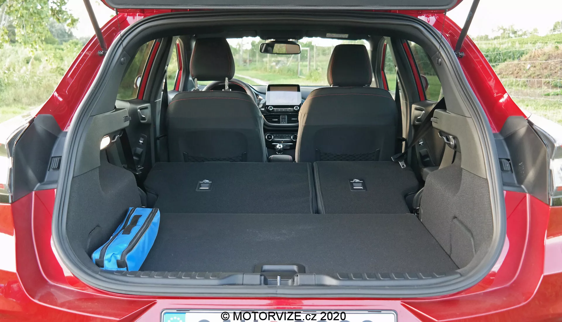 Image de l'aire de chargement de la Ford Puma 2020 vue de l'arrière, montrant le coffre ouvert avec les sièges arrière rabattus, un sac bleu à droite et un cache-bagages rétractable vertical à gauche, mettant en avant l'espace de rangement adaptable de la berline
