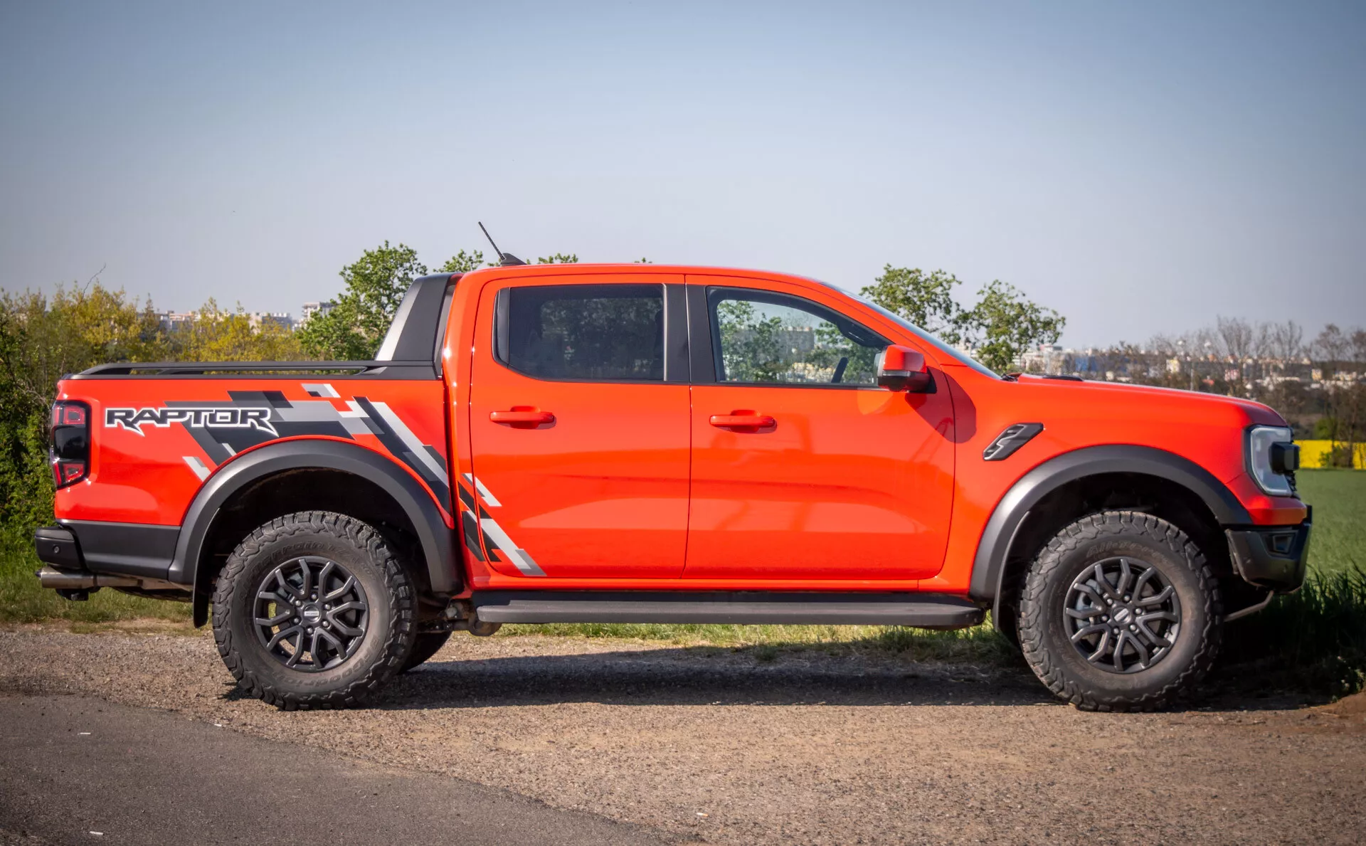 Ford Ranger Raptor 2022 en orange vif, présentant un style agressif, des capacités tout-terrain avec de grandes jantes noires et des pneus à gros crampons, garé sur une surface pavée à côté de l'herbe durant la journée