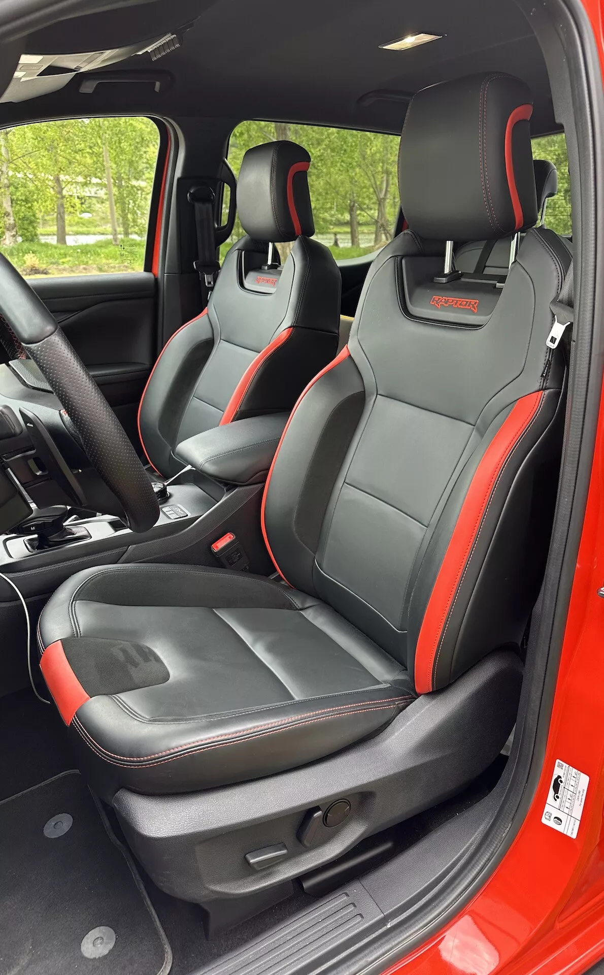 Vue intérieure du Ford Ranger 2022 se concentrant sur les sièges avant sportifs avec garniture d'accent noir et rouge, caractéristiques intégrées dans les appuie-tête et réglages électriques des sièges depuis une perspective latérale droite