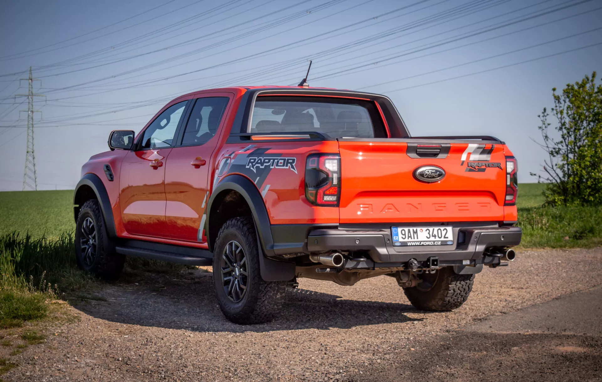 Pick-up Ford Ranger Raptor 2022 exposé sur un chemin de gravier, illustrant son angle arrière robuste de trois quarts avec un accent sur les capacités tout-terrain et une finition de peinture orange vibrante.