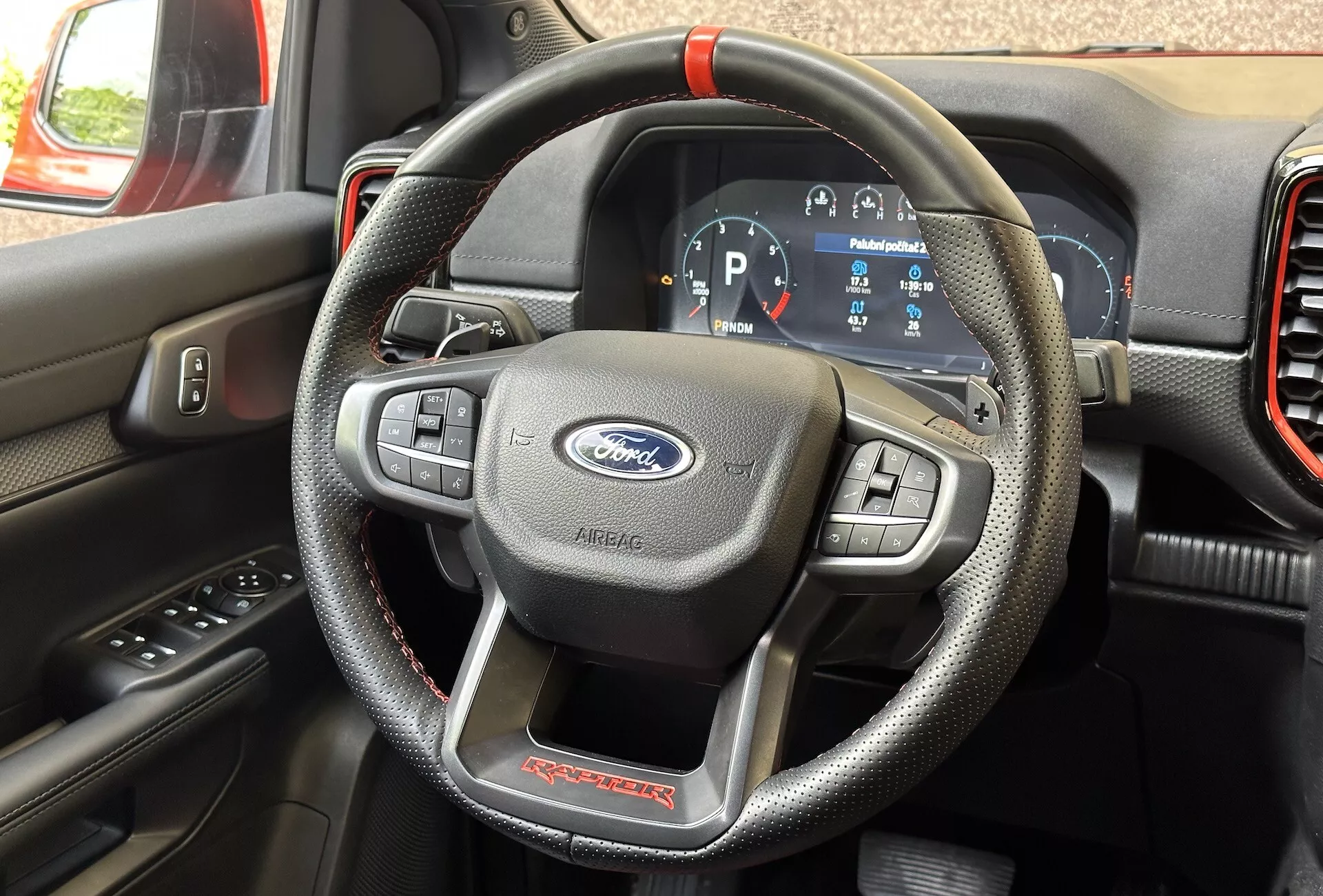 Vue détaillée de l'intérieur d'un Ford Ranger Raptor 2022 centrée sur le volant en matériau imitation cuir avec coutures rouges et commandes multifonctions, et le tableau de bord numérique montrant le véhicule en mode Parking.