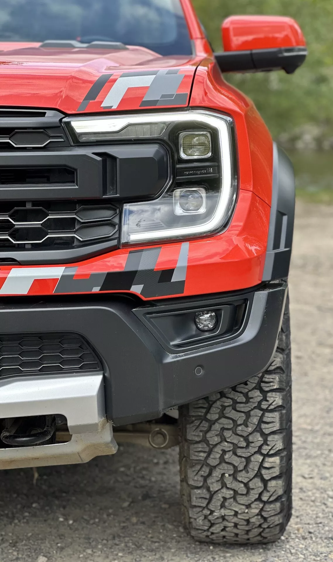 Vue rapprochée d'un camion pickup Ford Ranger 2022 en rouge, montrant le phare LED, la grille robuste, l'aile avant musclée avec décalcomanie et le motif de la bande de roulement pour tout-terrain depuis un angle bas pour souligner la robustesse et la technologie avancée
