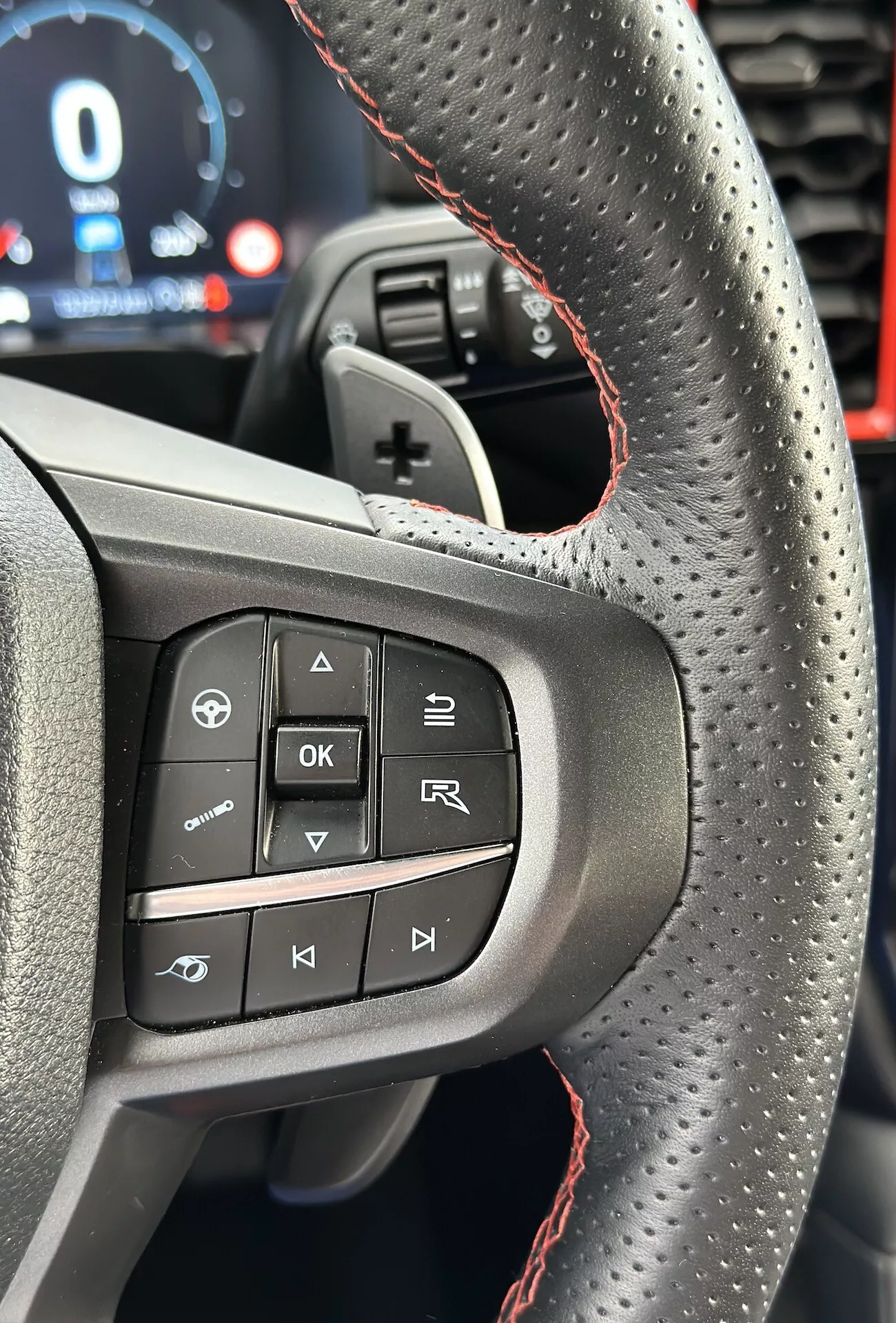 Gros plan sur le volant du Ford Ranger 2022 mettant en évidence les boutons et caractéristiques du côté gauche, y compris le cuir perforé avec coutures rouges, du point de vue du conducteur en orientation portrait