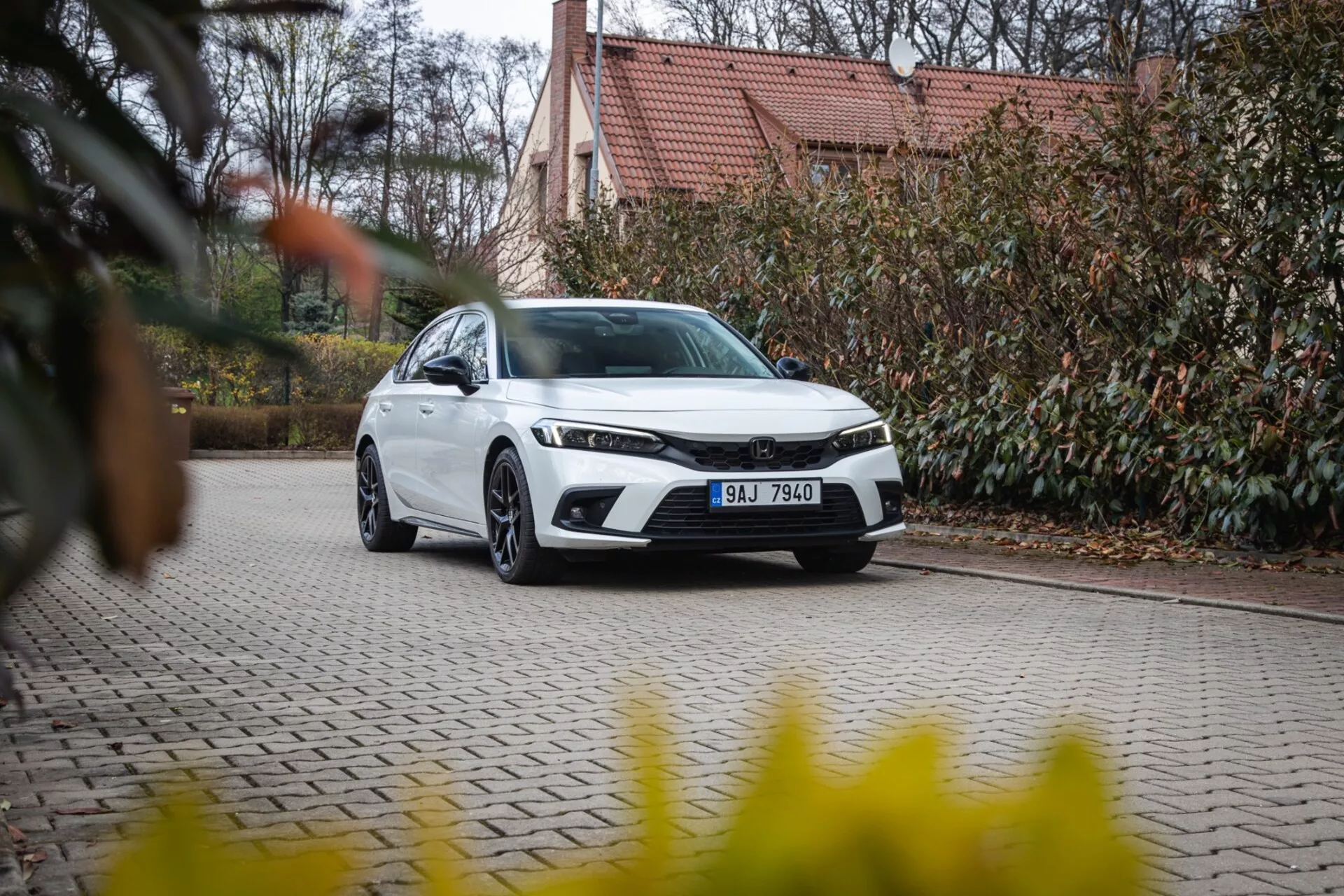 Sedan moderne Honda Civic 2022 garé sur une allée pavée avec aménagement paysager et bâtiment en arrière-plan, présentant calandre avant, phares LED et design aérodynamique élégant