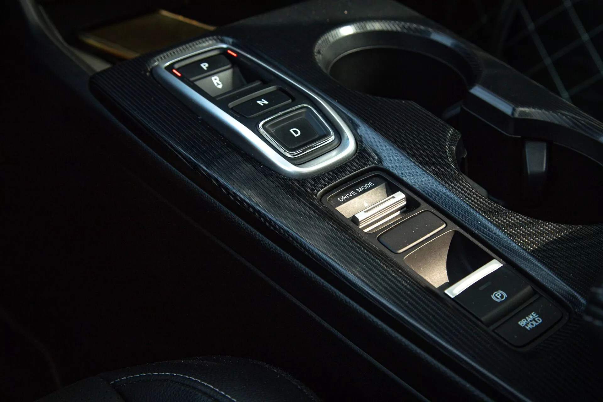 Gros plan de l'intérieur de la Honda Civic 2022 sur la console centrale avec sélecteur de vitesse électronique avec boutons 'P, R, N, D', panneau à texture de fibre de carbone et commandes auxiliaires, montrant la transmission automatique moderne et esthétique sportive