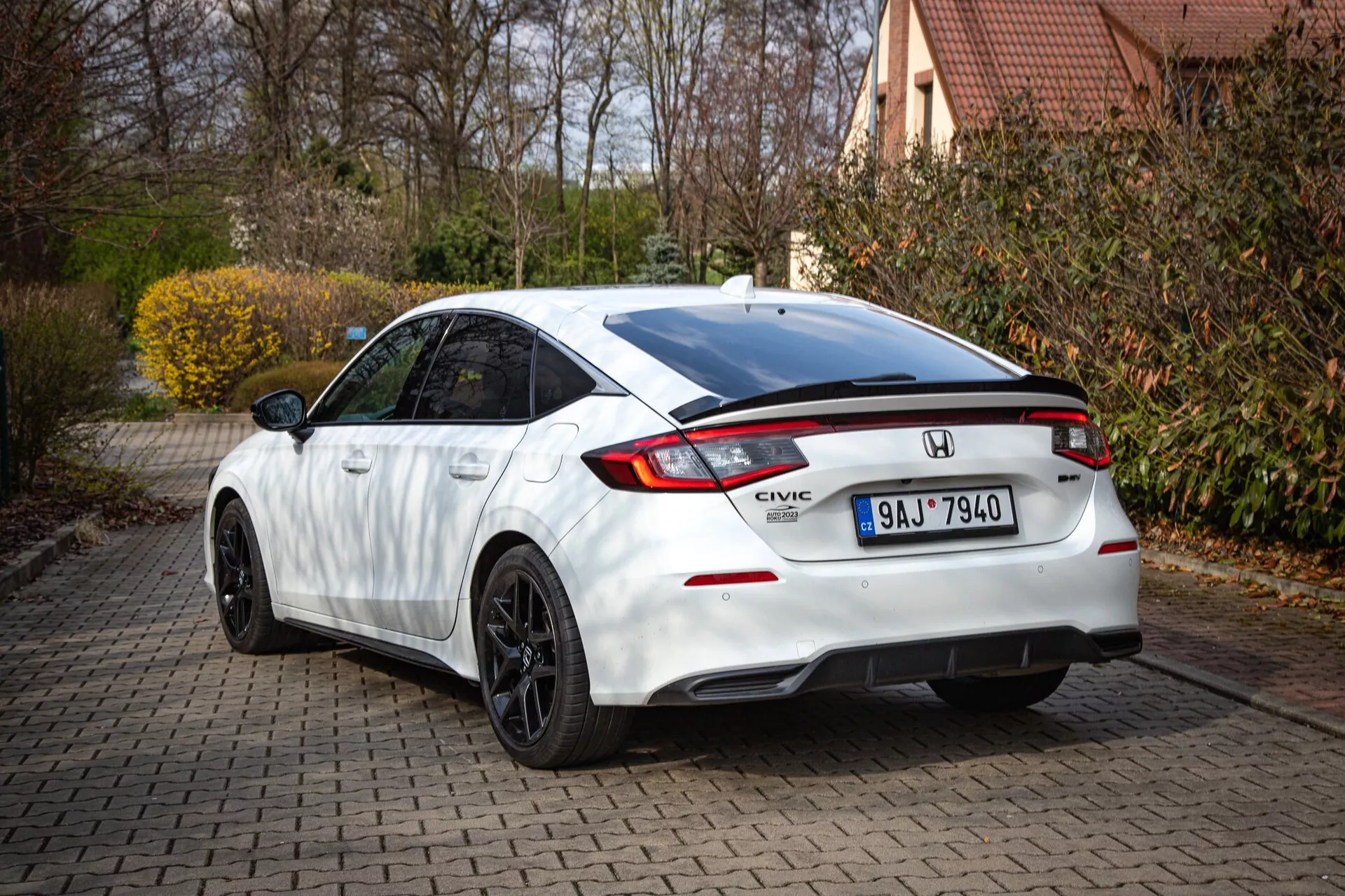 Honda Civic blanche 2022 montrant le profil arrière et partiel latéral sur une allée en briques, avec toit incliné, aileron intégré, feu de freinage LED, feux arrière distinctifs et pare-chocs sportif avec diffuseur
