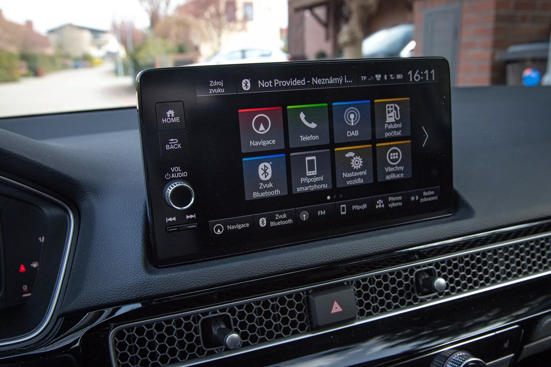 Intérieur de la Honda Civic 2022 montrant le système d'infodivertissement tactile moderne avec navigation, icônes de lecture audio et média, connectivité téléphonique, DAB, statut de la voiture, options Bluetooth et réglages du véhicule, contre un tableau de bord texturé avec un motif en nid d'abeille.