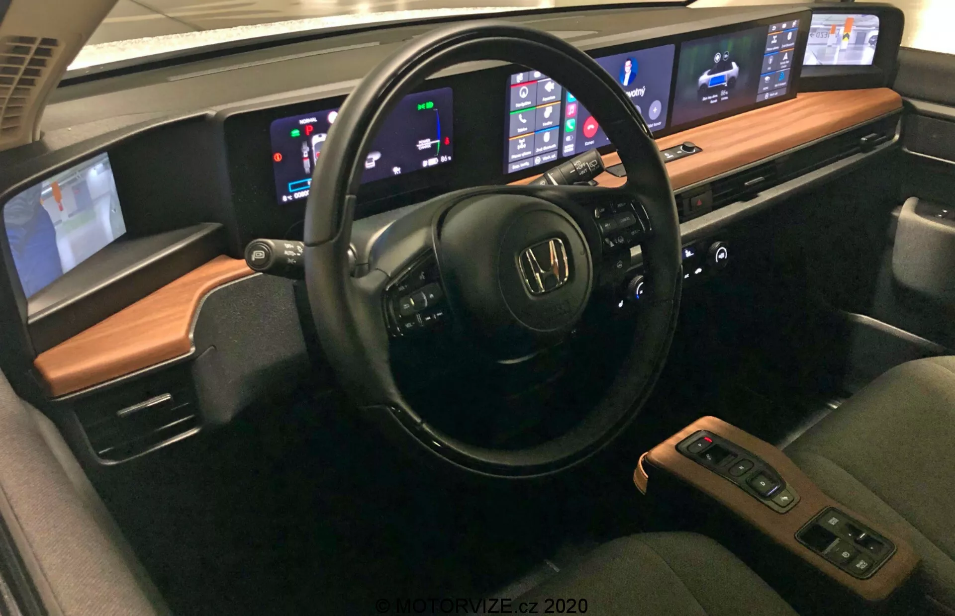 Intérieur de la Honda e 2020 présentant des caractéristiques avancées, notamment un volant multifonctions avec commandes audio et vocales, tableau de bord numérique affichant la vitesse et le niveau de carburant, système d'infodivertissement central compatible avec Apple CarPlay et Android Auto, contrôle automatique de la climatisation bi-zone, sièges confortables en cuir avec fonctions chauffantes, console centrale avec levier de vitesses et espace de rangement, systèmes avancés d'assistance à la conduite, options de connectivité comme ports USB et charge sans fil, système audio de haute qualité et éclairage d'ambiance personnalisable.