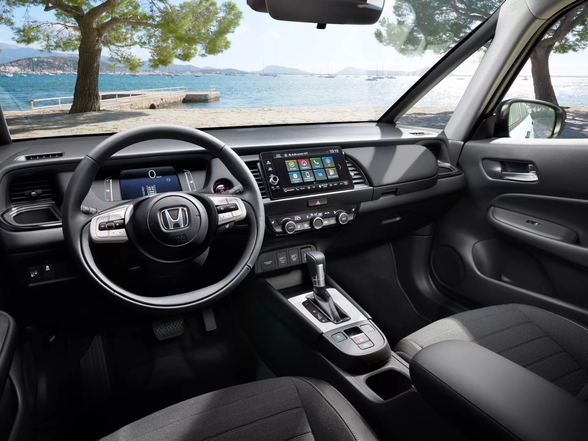 Vue rapprochée de l'intérieur de la Honda Jazz 2023 (5ème génération, facelift), se concentrant sur son volant multifonction moderne en cuir, tableau de bord numérique, système d'infodivertissement tactile, commande de climatisation, levier de vitesse automatique, sièges en tissu et matériaux de qualité supérieure du point de vue du passager avant.