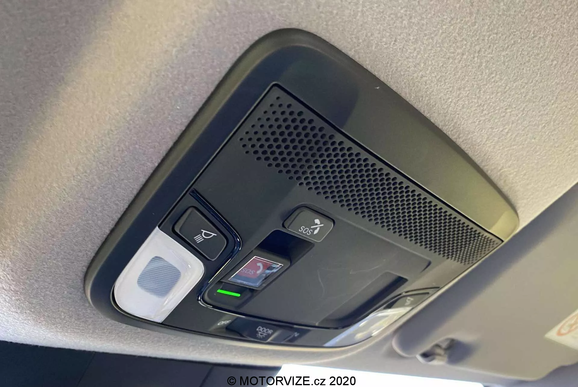 Vue rapprochée de la console supérieure du Honda Jazz 2020 (Jazz Crosstar). L'image révèle une série de boutons fonctionnels, y compris des commandes de lumière intérieure, un possible bouton de déverrouillage de porte, une zone ventilée avec un microphone pour appels mains libres, un home link avec des boutons programmables pour l'ouverture de garage et un possible compartiment pour lunettes de soleil ou un loquet de rangement. La console est capturée en plein jour avec une mise au point nette sur les boutons texturés, mettant en évidence la technologie avancée et le design intérieur du véhicule.