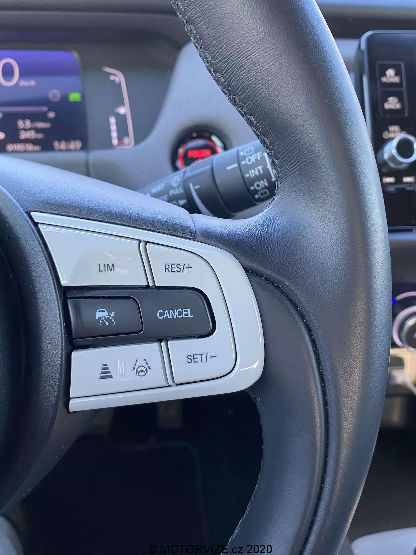 Vue détaillée des commandes du volant de la Honda Jazz 2020 Crosstar, mettant en avant les boutons et fonctionnalités du côté gauche tels que LIM (limiteur de vitesse), RES/+ (reprendre ou augmenter la vitesse), CANCEL et SET/- (régler ou diminuer la vitesse). L'image est prise du point de vue du conducteur, mettant en évidence un volant en cuir noir avec des finitions mates et brillantes, et montrant des icônes liées au régulateur de vitesse et à d'éventuels systèmes avancés d'aide à la conduite.