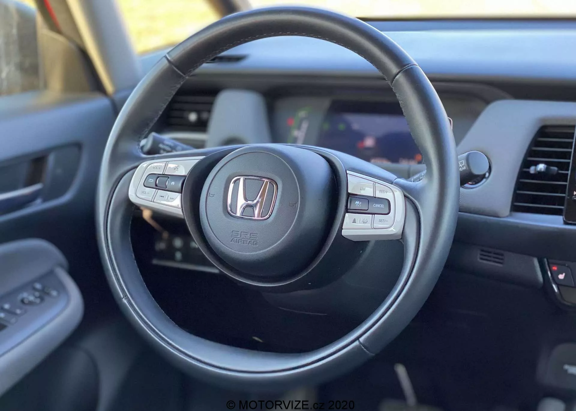 Vue intérieure de la Honda Jazz Crosstar 2020 depuis la perspective du conducteur, mettant en avant le volant moderne avec logo Honda, doté de boutons de contrôle multifonctions pour l'audio, le régulateur de vitesse et les appels mains libres, avec une vue partielle du tableau de bord et du système d'infodivertissement.