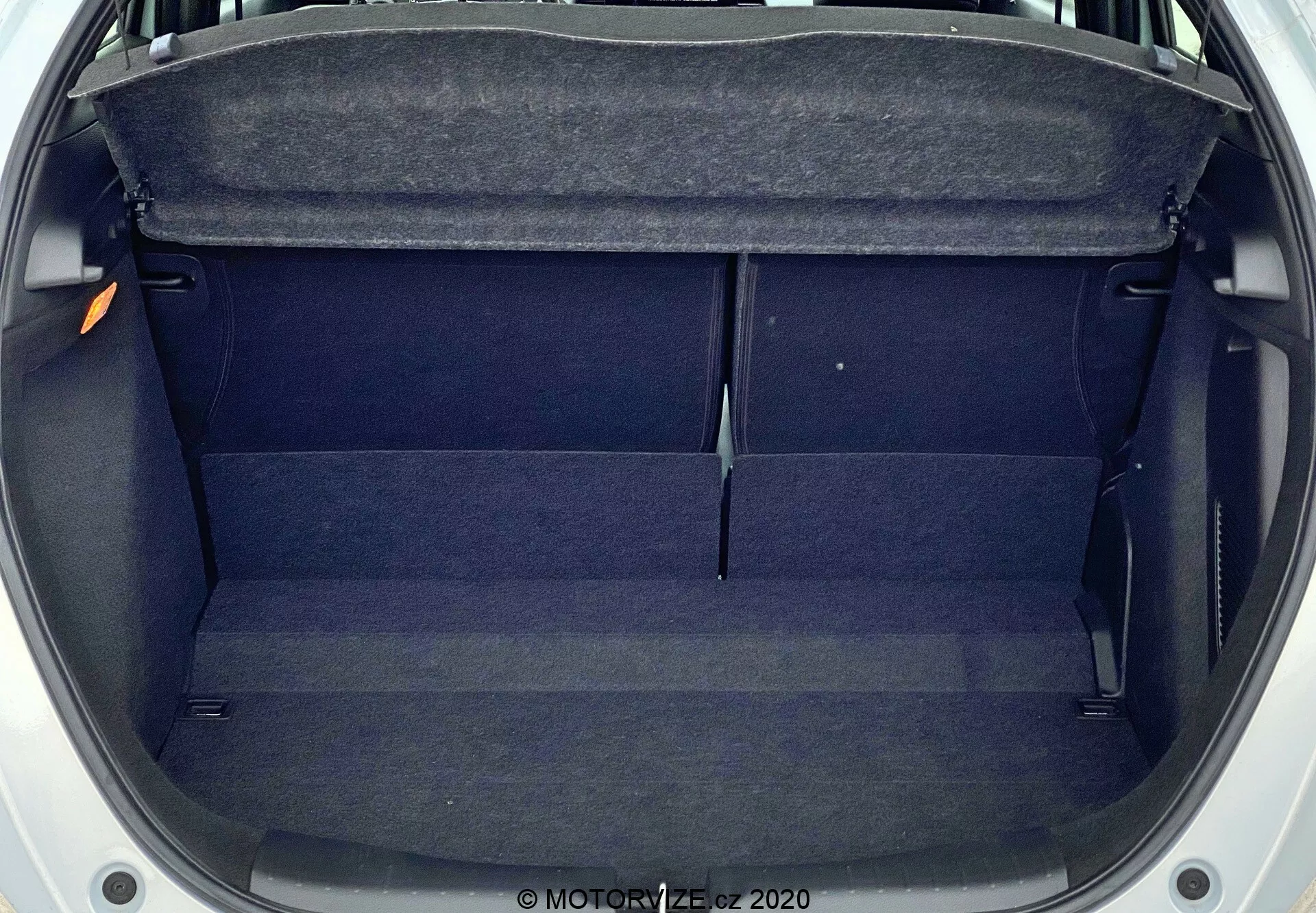 Vue aérienne du coffre vide de la Honda Jazz 2020, montrant un espace rectangulaire de taille moyenne avec un revêtement en tissu sombre. Les caractéristiques incluent une étagère en haut, des garnitures intérieures sur les côtés et une légère élévation au centre. Le coffre est propre, non obstrué et semble bien entretenu.