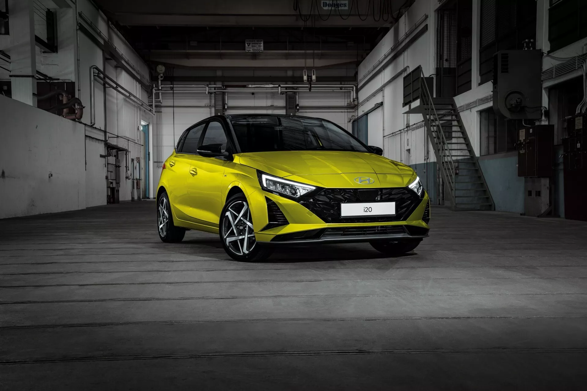 Hyundai i20 2023 (3ème génération face-lift) vue de trois quarts avant montrant son design moderne de hatchback, phares LED, pare-choc avant sportif et jantes en alliage à l'intérieur d'un entrepôt industriel avec sol en béton et portes métalliques