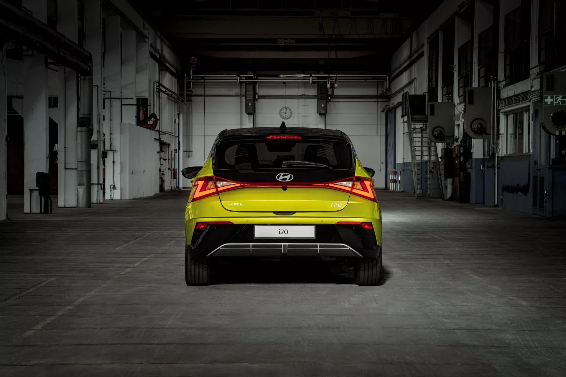 Vue arrière d'une Hyundai i20 2023 (3e génération-facelift) hatchback avec feux arrière LED et assistance au stationnement, mise en évidence dans un cadre industriel
