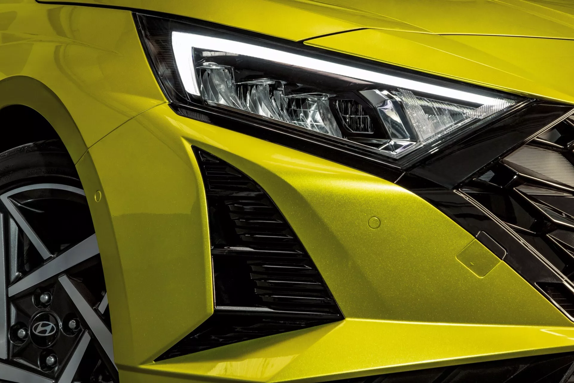 Vue du quart avant gauche de la Hyundai i20 2023, mettant en évidence ses lignes de design agressives, phare LED avancé, capot jaune métallique, aile avant aérodynamique avec prises d'air, et roue en alliage sportive avec système de freinage performant
