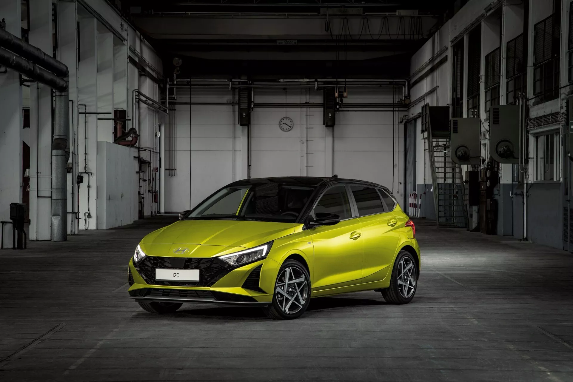 Hyundai i20 3ème génération facelift 2023 photographiée sous un angle avant trois quarts, montrant ses phares LED élégants, sa grille avant sportive et sa couleur jaune vif sur un fond industriel, mettant en valeur son design contemporain et ses caractéristiques technologiques.