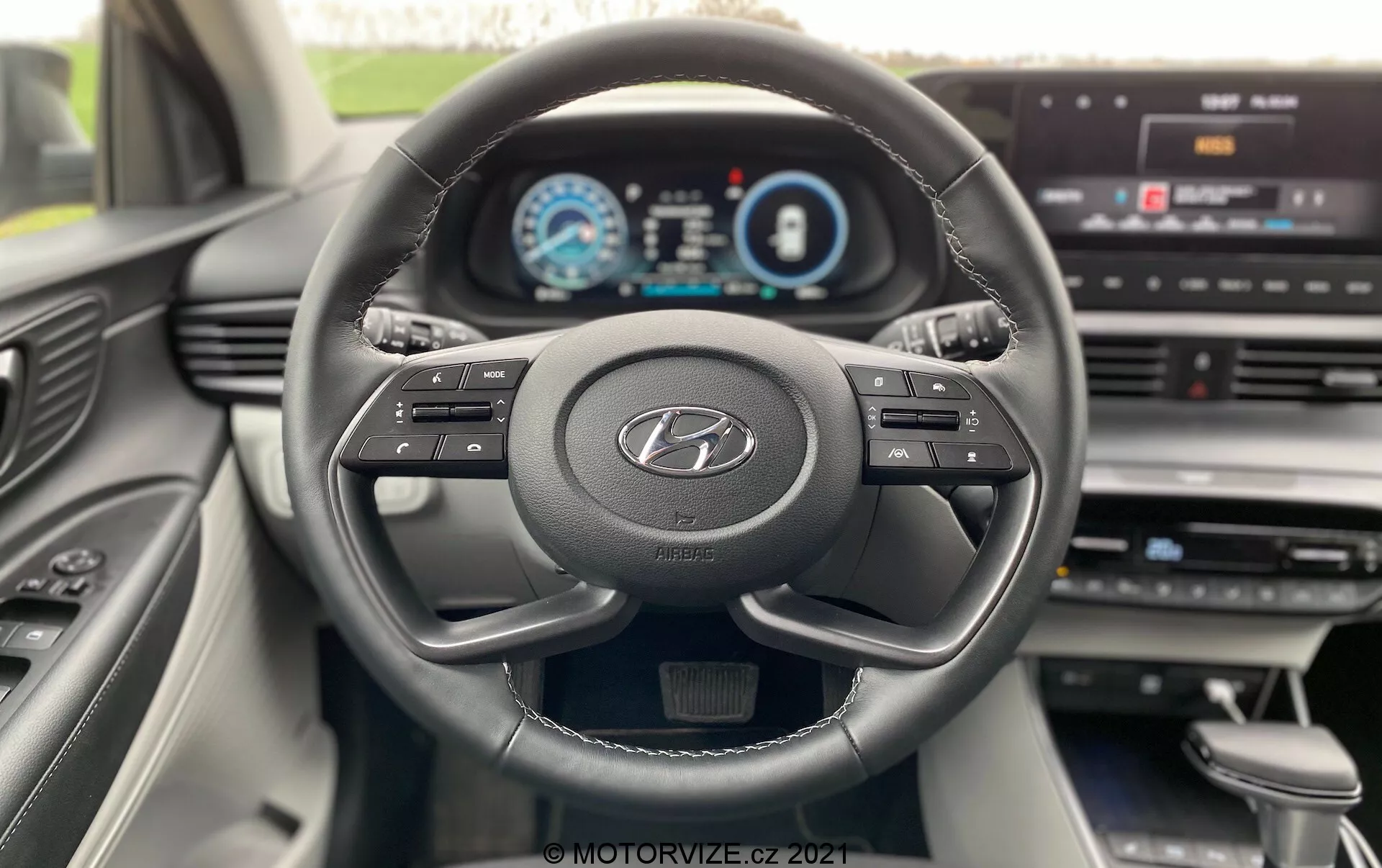 Vue intérieure de la Hyundai i20 2020 depuis la perspective du conducteur, montrant un volant moderne à trois branches avec le logo Hyundai, des boutons multifonctions et un tableau de bord entièrement numérique affichant le compteur de vitesse, le compte-tours et l'écran d'information du conducteur. Le tableau de bord comporte un écran central d'infodivertissement avec des options de menu, indiquant une intégration technologique avancée et une interface conviviale. Le design intérieur est moderne, avec des lignes épurées et des matériaux de qualité visibles dans la console centrale et la porte côté passager.