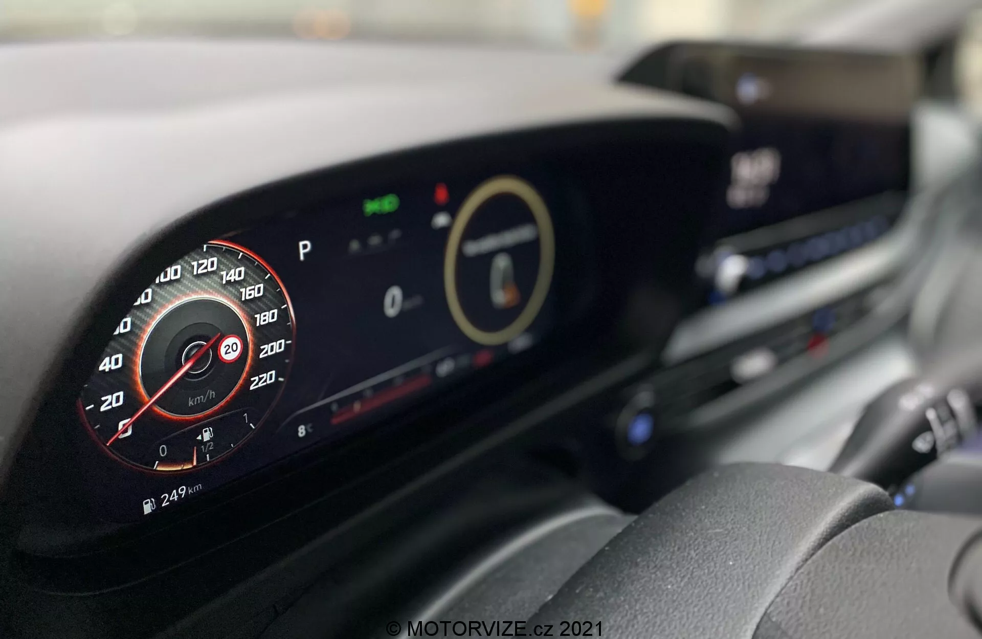 Intérieur de la Hyundai i20 2020 avec un tableau de bord moderne. Image prise depuis le siège du conducteur avec un accent sur le tableau de bord numérique et l'affichage central, montrant des détails comme un tachymètre analogique simulé, des indicateurs écologiques et un système d'infodivertissement. D'autres fonctionnalités comme les bouches d'aération et les boutons de commande du climat sont également visibles.