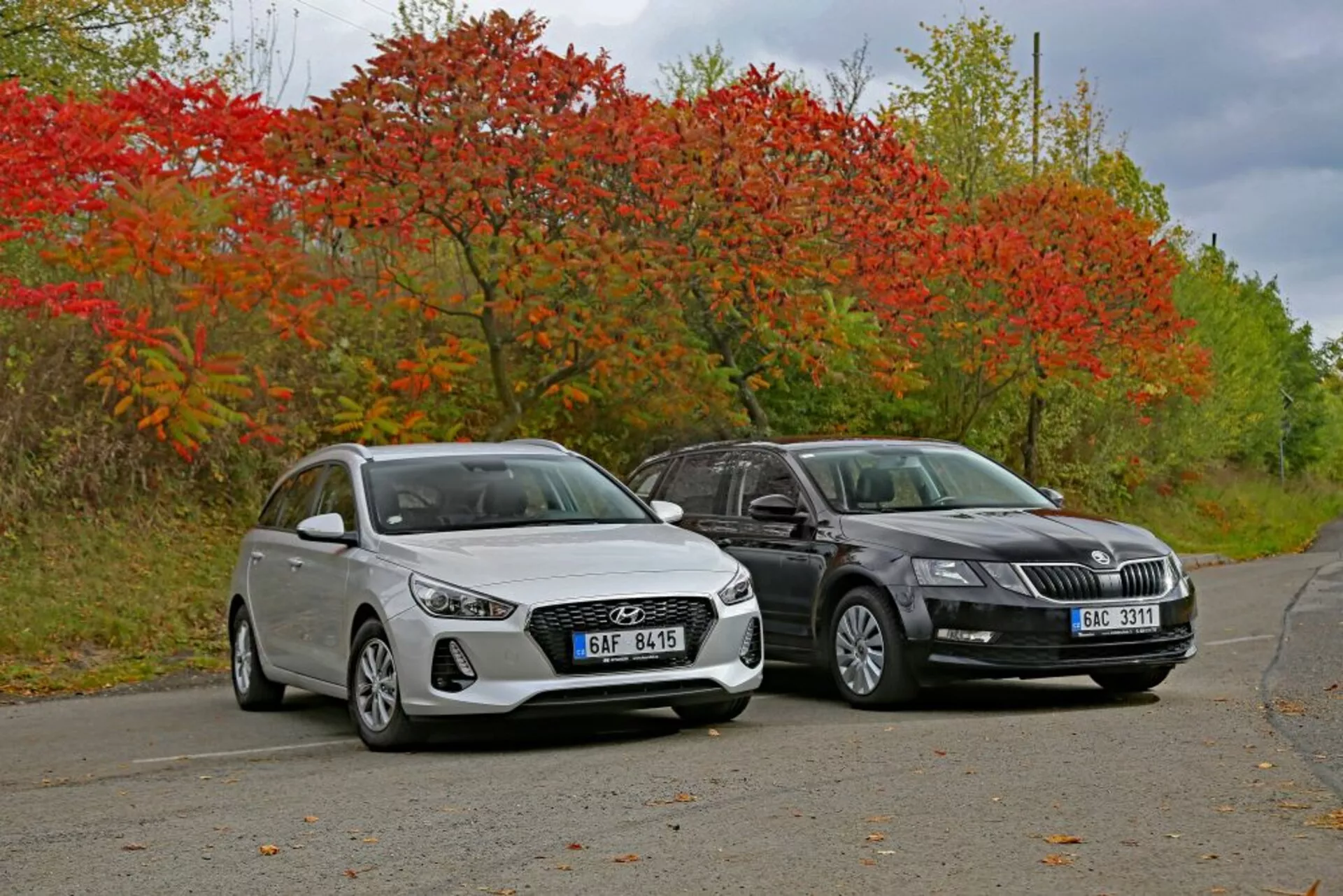 Hyundai i30 hatchback blanche de 2017 et berline de couleur foncée côte à côte sur une route calme entourée de végétation automnale, présentant des lignes de design et une technologie d'éclairage moderne