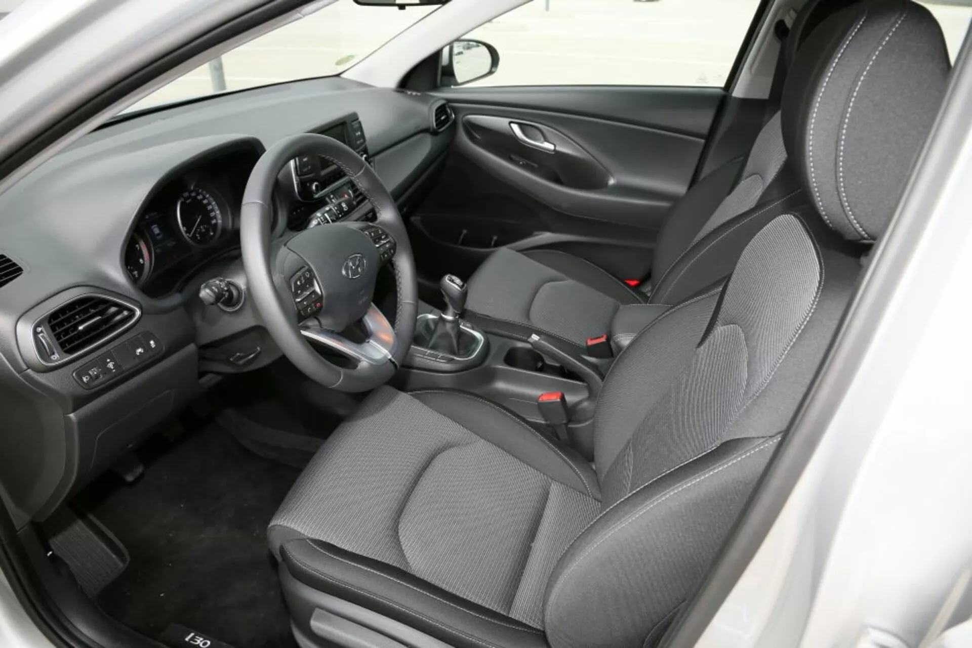 Vue intérieure de la Hyundai i30 2017 (i30-N) axée sur l'habitacle avant, présentant le siège du conducteur avec commandes au volant, levier de vitesse manuel, console centrale et sièges en tissu à motifs