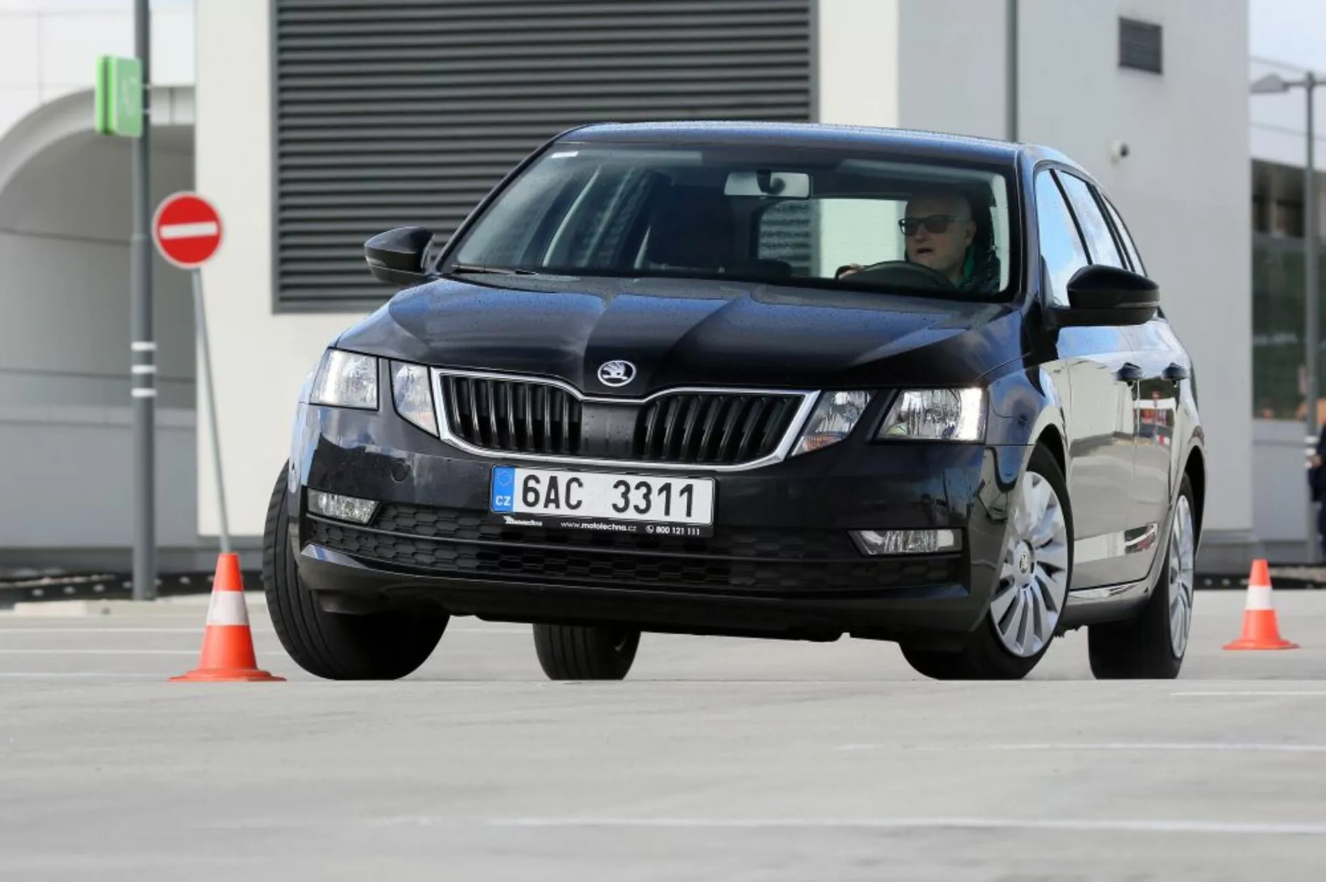 Sedan noir Hyundai i30 de 2017 à quatre portes naviguant autour de cônes de circulation orange démontrant la maniabilité du véhicule, vue avant-trois-quarts avec le logo du fabricant visible sur la calandre et des phares halogènes ou au xénon sans motifs LED, technologie traditionnelle des essuie-glaces, roues floues indiquant un mouvement, et sans accessoires de luxe visibles ni fonctionnalités technologiques avancées, dans un établissement d'essai pavé