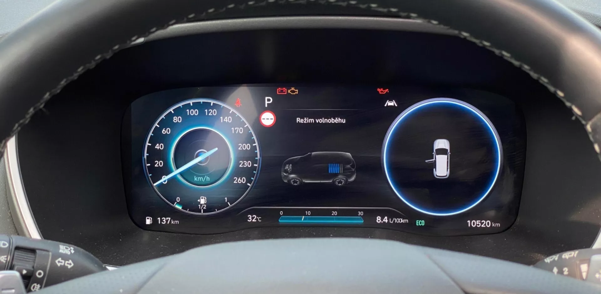 Vue rapprochée du tableau de bord numérique moderne d'une Hyundai Santa Fe 2020, prise depuis la perspective du conducteur. Focalisée sur la zone du tableau de bord, l'image comporte deux écrans numériques principaux, bleu et noir. L'écran de gauche est un compteur de vitesse affichant 137 km/h avec des indicateurs de RPM supplémentaires. L'écran de droite surveille l'état du véhicule, incluant une alerte de maintenance et un avertissement 'Maintenir visibilité'. La section inférieure montre la température extérieure (3,2°C) et l'odomètre (10.520 km), ainsi qu'un indicateur d'efficacité de 8,4 litres par 100 kilomètres.