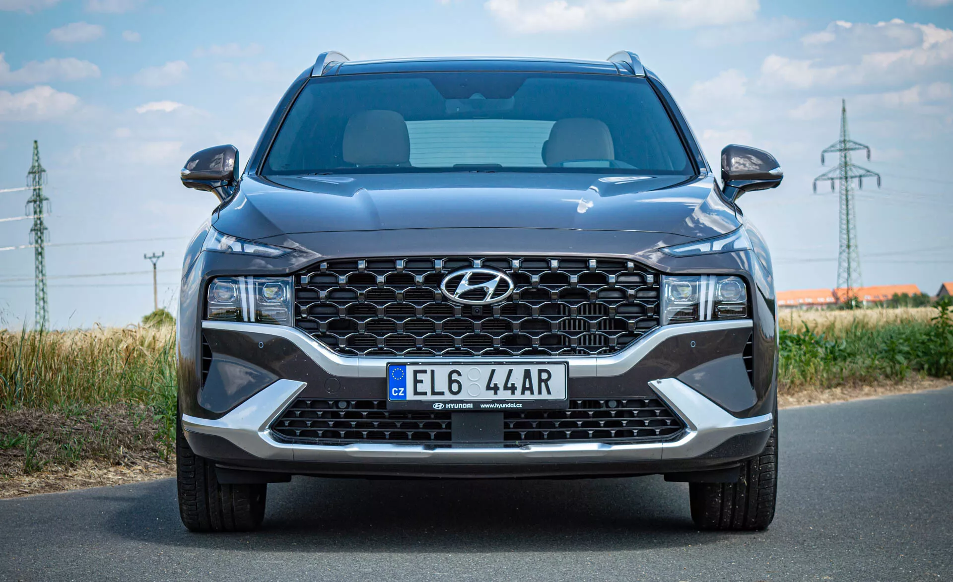 Vue frontale d'un SUV moderne Hyundai Santa Fe 2020 prise en plein jour. L'image montre une grande calandre en cascade avec le logo central de Hyundai, une plaque d'immatriculation de style européen, des phares à LED angulaires élégants, une large prise d'air centrale et des accents argentés sur le pare-chocs inférieur. Les lignes sculptées du capot, le pare-brise partiel et les rétroviseurs latéraux avec clignotants intégrés sont visibles. L'image met en évidence la taille de la voiture, en détaillant son design moderne et ses caractéristiques technologiques.