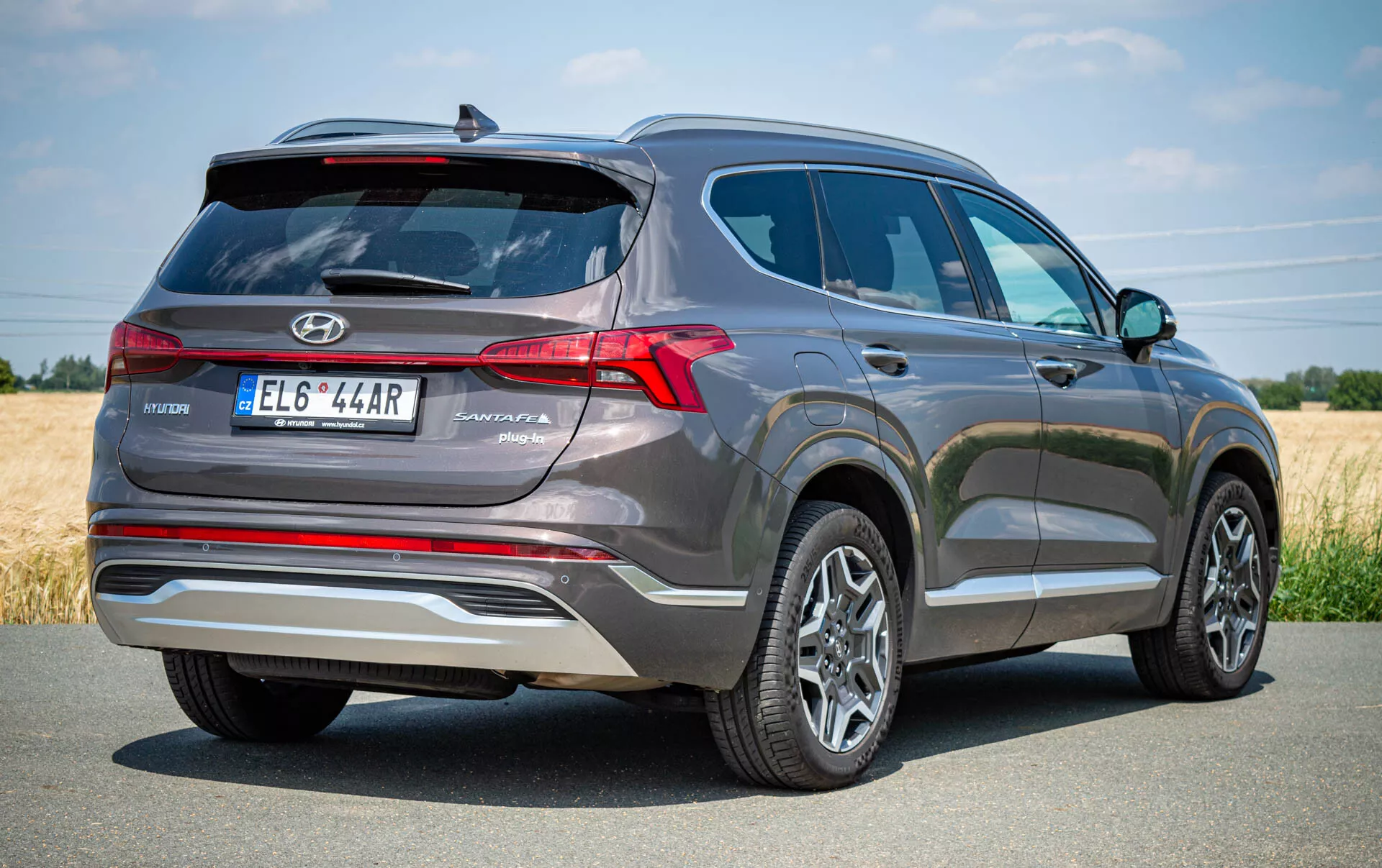 Vue arrière trois-quarts d'un SUV Hyundai Santa Fe 2020 gris, mettant en avant le côté arrière gauche. L'image montre des feux arrière LED proéminents, un lave-glace arrière, un dégivreur et un essuie-glace, avec l'emblème Hyundai et le nom du modèle 'Santa Fe' près de la plaque d'immatriculation centrée. Une garniture argentée ajoute une touche de style et une caméra de recul ou un système de capteurs se trouve au-dessus de la plaque. Les roues en alliage à multiples rayons et les pneus en bon état sont également visibles, indiquant un véhicule moderne et bien entretenu. Idéal pour les listings automobiles, les critiques ou le contenu axé sur la technologie.