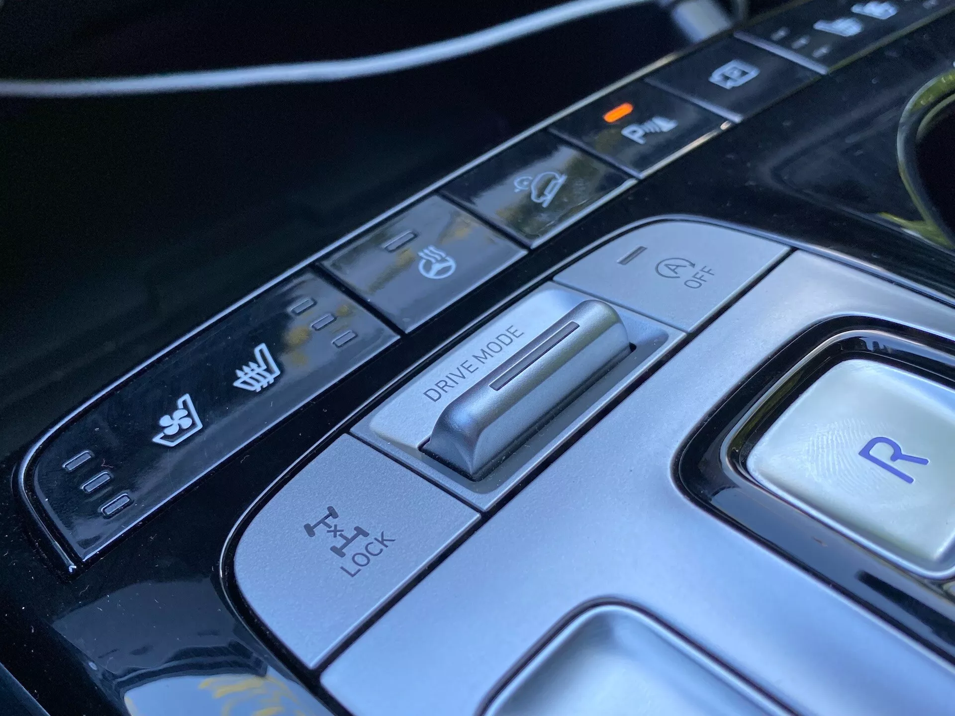 Vue rapprochée de la console centrale de la Hyundai Tucson 2020, mettant en avant le sélecteur de mode de conduite et divers boutons de commande. L'image révèle un sélecteur de mode de conduite avancé pour différentes conditions de conduite, un panneau de commande de traction, un bouton pour la marche arrière et des contrôles supplémentaires pour la stabilité du véhicule et les fonctions d'assistance au stationnement. Le design élégant et les matériaux de haute technologie mettent en avant l'intérieur sophistiqué de cette voiture de luxe moderne.