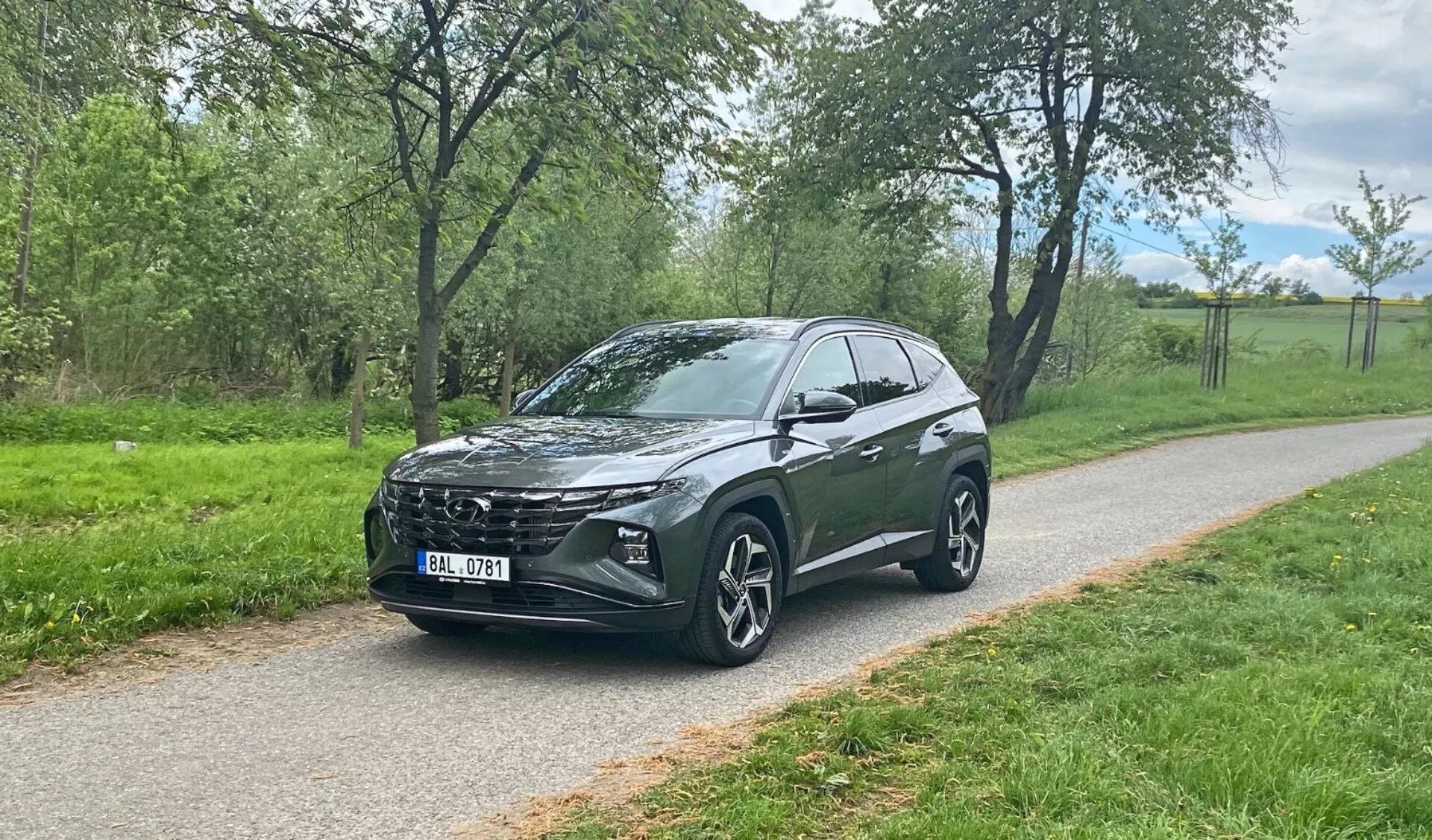 Vue avant trois-quarts d'un SUV crossover Hyundai Tucson 2020 garé sur un chemin pavé avec de la verdure en arrière-plan, présentant la calandre distinctive du véhicule, les phares à LED modernes, les grandes roues en alliage multi-branches, la ligne de toit inclinée, la garde au sol élevée, les rétroviseurs intégrés, le vitrage teinté et les contours stylés de la carrosserie.