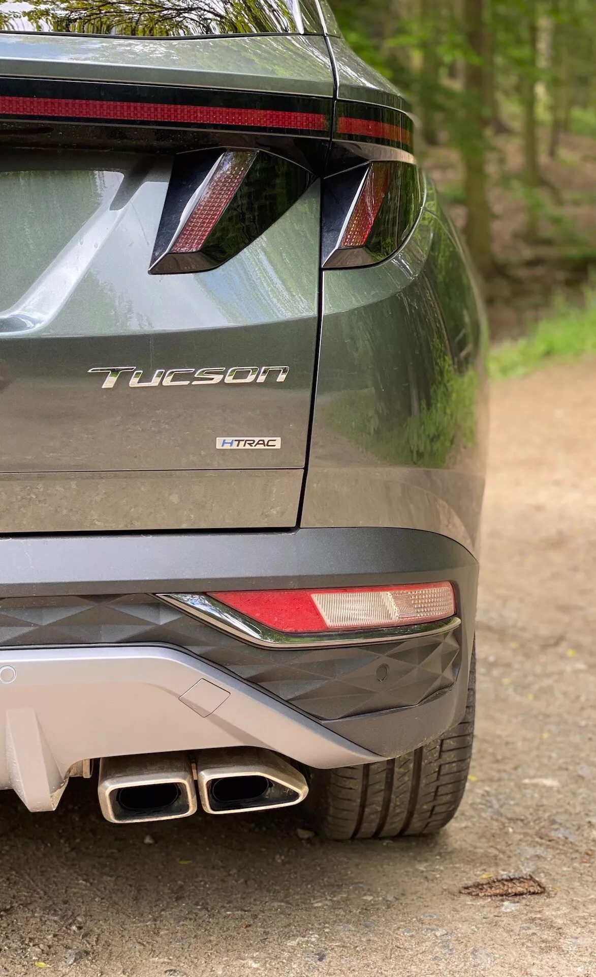Vue partielle arrière du modèle Hyundai Tucson 2020 indiquant qu'il s'agit de la version 1.6 T-GDi Pure, montrant le côté droit du pare-chocs, un feu arrière partiel, un aileron arrière avec feu de freinage LED, des doubles embouts d'échappement et un badge de modèle avec le nom 'Tucson' et la technologie moteur 'T-GDi'.