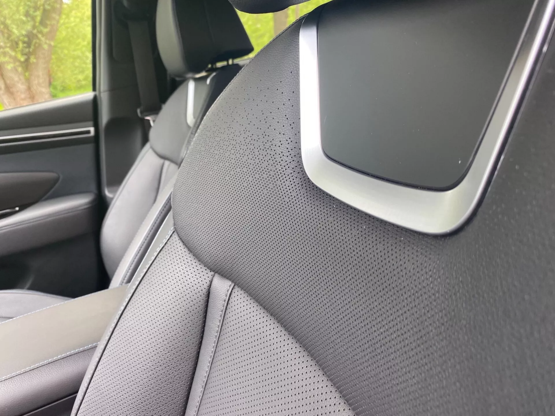 Gros plan de l'intérieur de la Hyundai Tucson 2020 axé sur le montant A côté droit et une partie du siège avant droit. Le montant A est recouvert d'un matériau texturé, probablement en tissu ou en similicuir, suggérant un accent sur l'esthétique ou la réduction du bruit. Le siège a un design bicolore et est perforé pour la ventilation. Un élément notable à la jonction du montant A et du plafond pourrait faire partie du système audio, d'un composant d'airbag ou d'un capteur d'assistance à la conduite, soulignant des fonctionnalités avancées de sécurité ou de technologie.