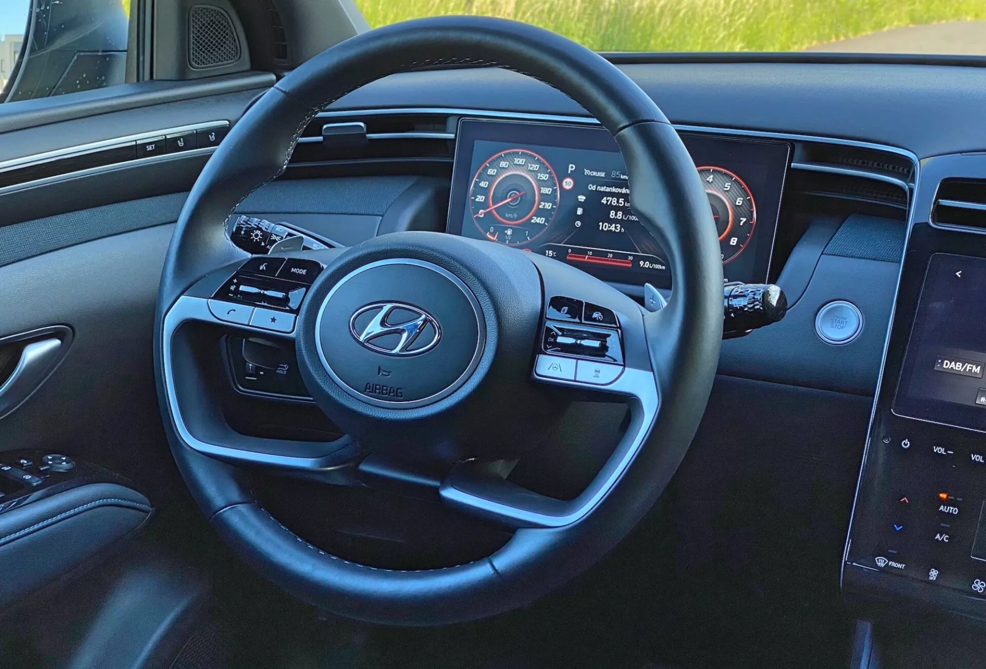 Vue intérieure du Hyundai Tucson 1.6 T-GDI 2020 depuis la perspective du conducteur, centrée sur le volant moderne à trois branches avec logo Hyundai, boutons de contrôle des médias et du régulateur de vitesse, tableau de bord partiellement visible avec compteur de vitesse et compteur de régime, et système d'infodivertissement central à écran tactile sur le tableau de bord.