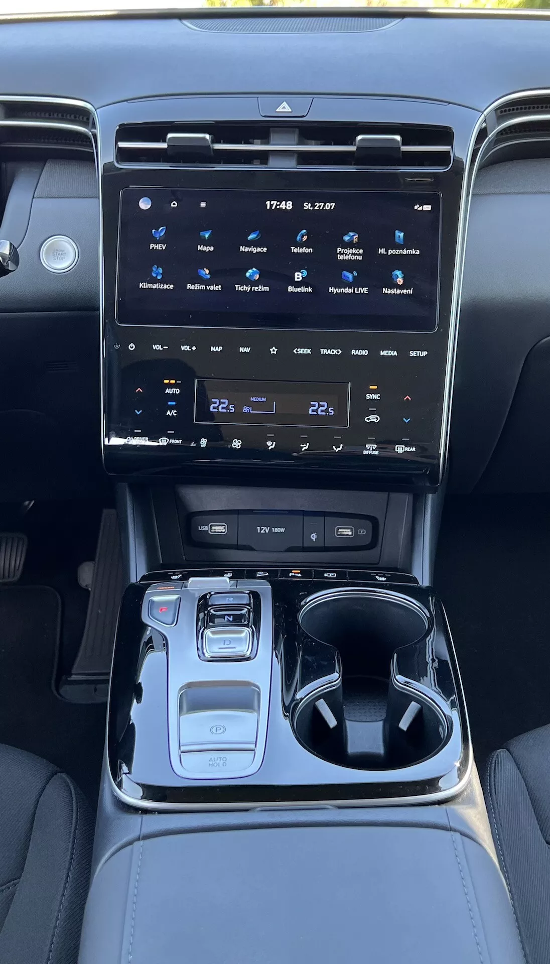 Intérieur du Hyundai Tucson 2020 montrant la console centrale avec un grand système d'infodivertissement tactile, boutons de contrôle climatique, sélecteur de vitesse électronique, sélecteur de mode de conduite, porte-gobelets, compartiment de rangement et éclairage d'ambiance.