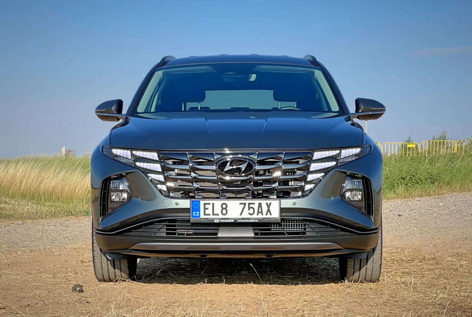 Vue de face du Hyundai Tucson 2020 présentant un design de capot aérodynamique, une grille en cascade, des phares LED pointus et un pare-chocs détaillé avec des caractéristiques technologiques possibles, situé sur un fond de paysage naturel