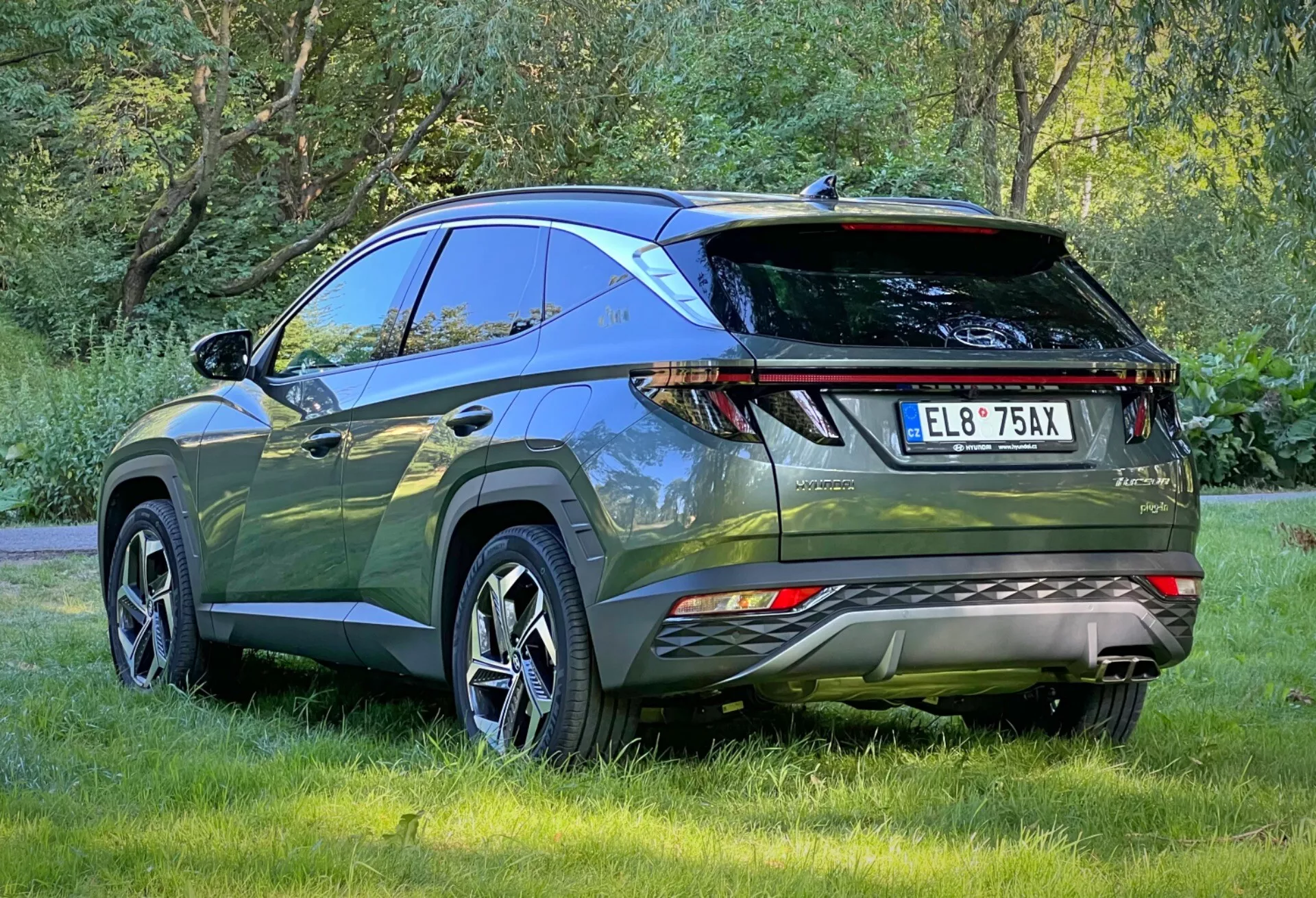 Vue arrière trois quarts de la Hyundai Tucson 2020 mettant en évidence les feux arrière LED, les capteurs de stationnement, les doubles échappements, le spoiler arrière sportif et les barres de toit, garée en extérieur sur l'herbe montrant la conception aérodynamique et les caractéristiques avancées d'un SUV crossover moderne pour l'aventure en plein air et l'utilisation pratique.