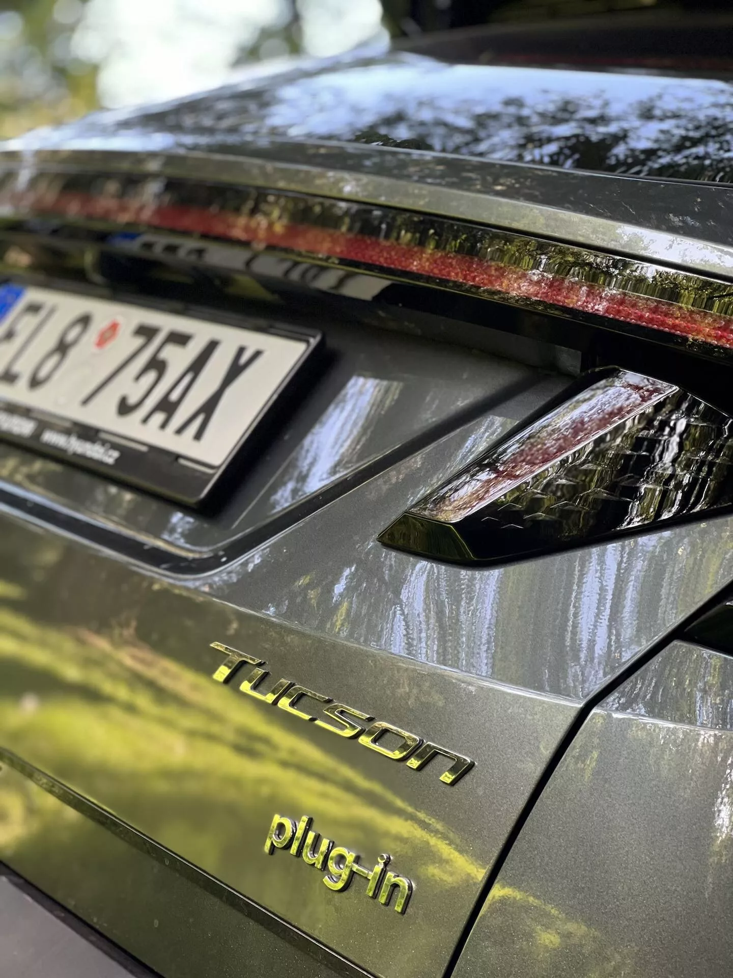 Vue rapprochée de la section arrière d'une Hyundai Tucson 2020 hybride rechargeable, mettant en vedette le couvercle du coffre, l'ensemble d'éclairage arrière avec des lumières LED, finition brillante foncée, et des détails indiquant des conditions de stationnement en extérieur