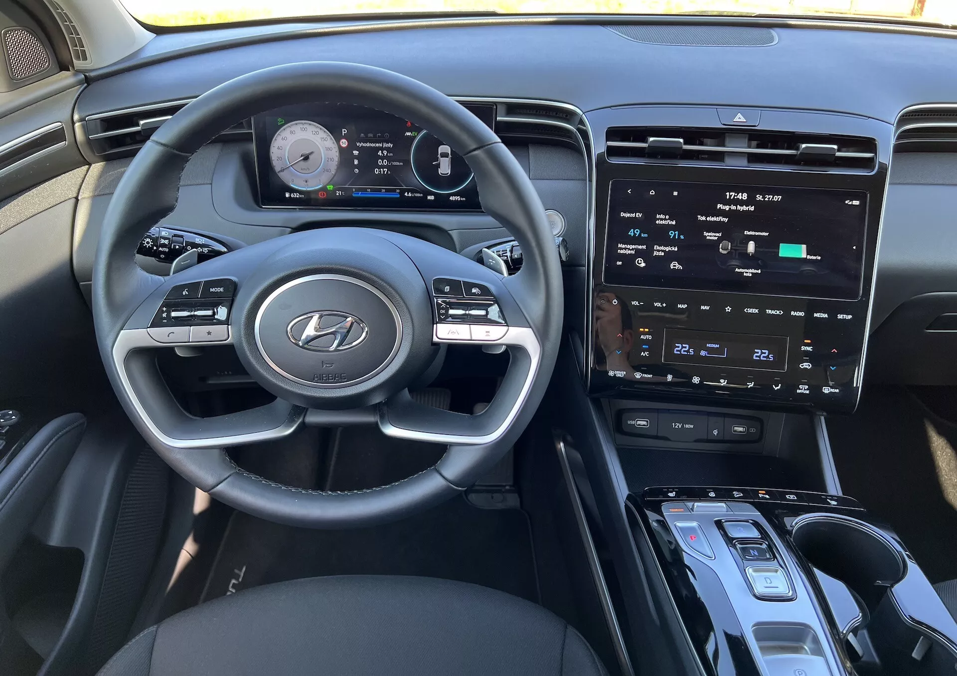 Intérieur du Hyundai Tucson 2020 montrant le volant avec logo Hyundai, tableau de bord numérique avancé, écran tactile central pour l'infodivertissement, commandes de climatisation, bouton de démarrage/arrêt, levier de vitesses et zone possible de charge sans fil du point de vue du conducteur