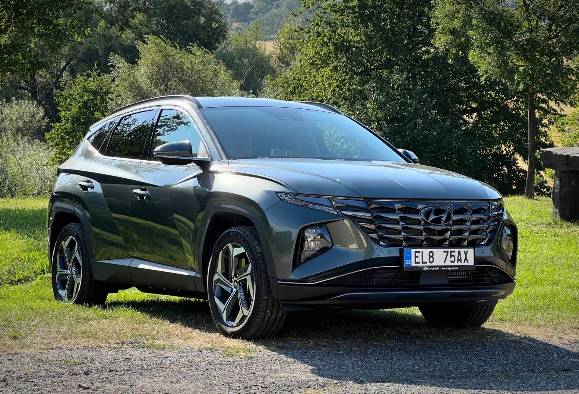 Hyundai Tucson 2020 garée sur l'herbe avec en arrière-plan la campagne, présentant une perspective avant aux trois quarts pour une vue détaillée de ses phares LED élégants, de sa grille avant angulaire et de sa finition brillante foncée