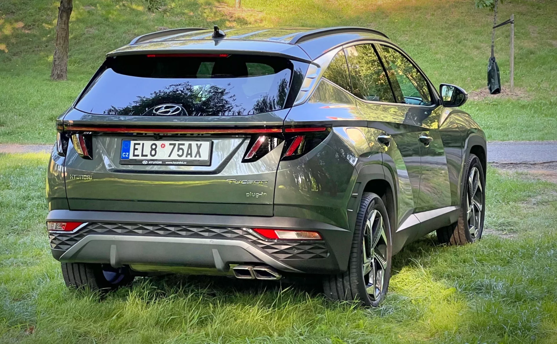 Vue arrière trois quarts du Hyundai Tucson 2020, présentant ses feux arrière LED, son design aérodynamique avec un aileron de toit et une antenne aileron de requin, sa finition premium en vert métallique foncé, et équipé de grandes roues en alliage et de capteurs de stationnement, dans un cadre de vie crossover urbain