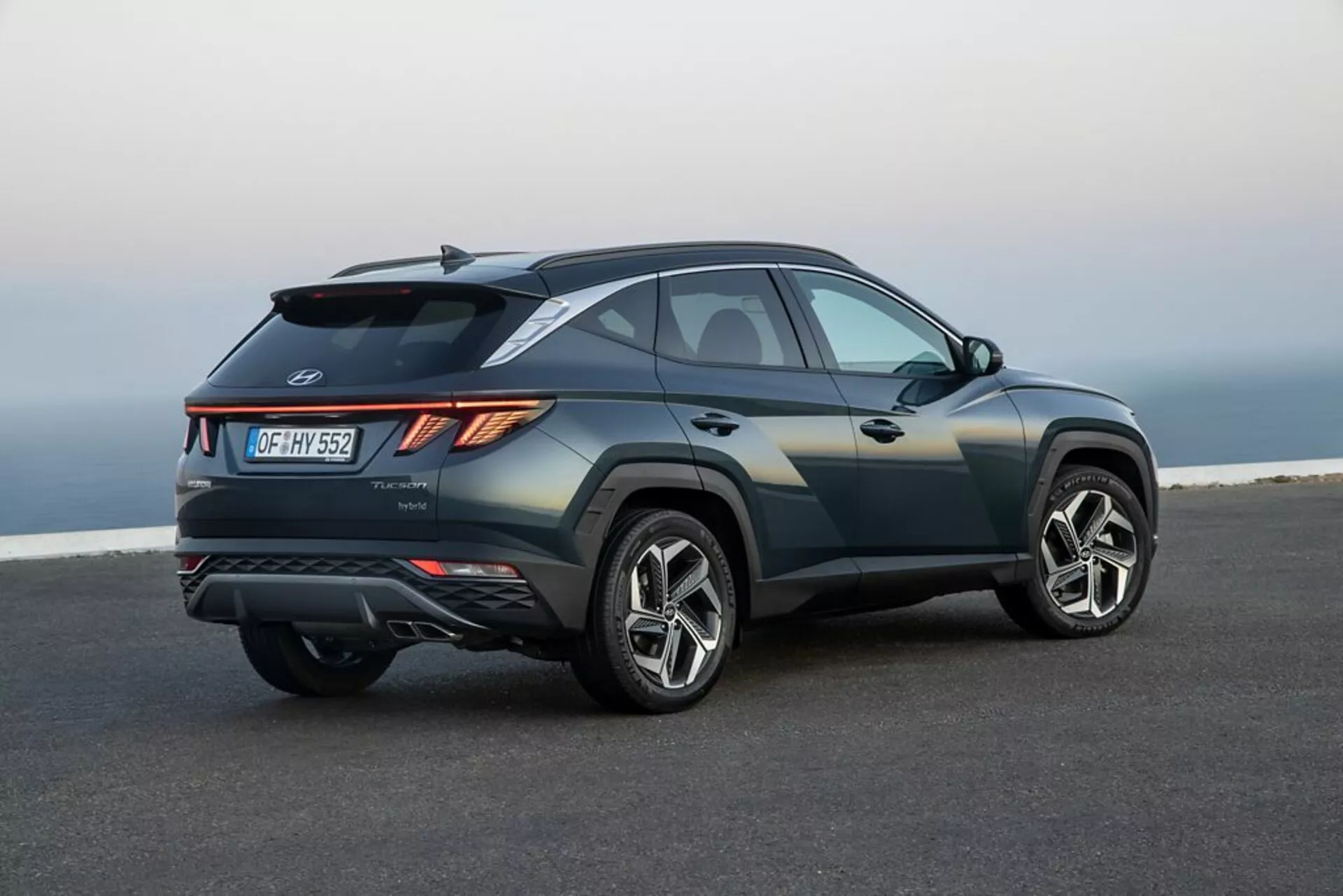 SUV Hyundai Tucson 2020 stationné sur du tarmac lisse avec un paysage côtier ou surélevé en arrière-plan, mettant en avant son design élégant et sportif, sa ligne de ceinture montante, sa ligne de toit inclinée, ses plis nets de carrosserie, ses feux arrière LED angulaires, son aileron arrière, son diffuseur intégré, ses doubles sorties d'échappement, et ses grandes roues en alliage